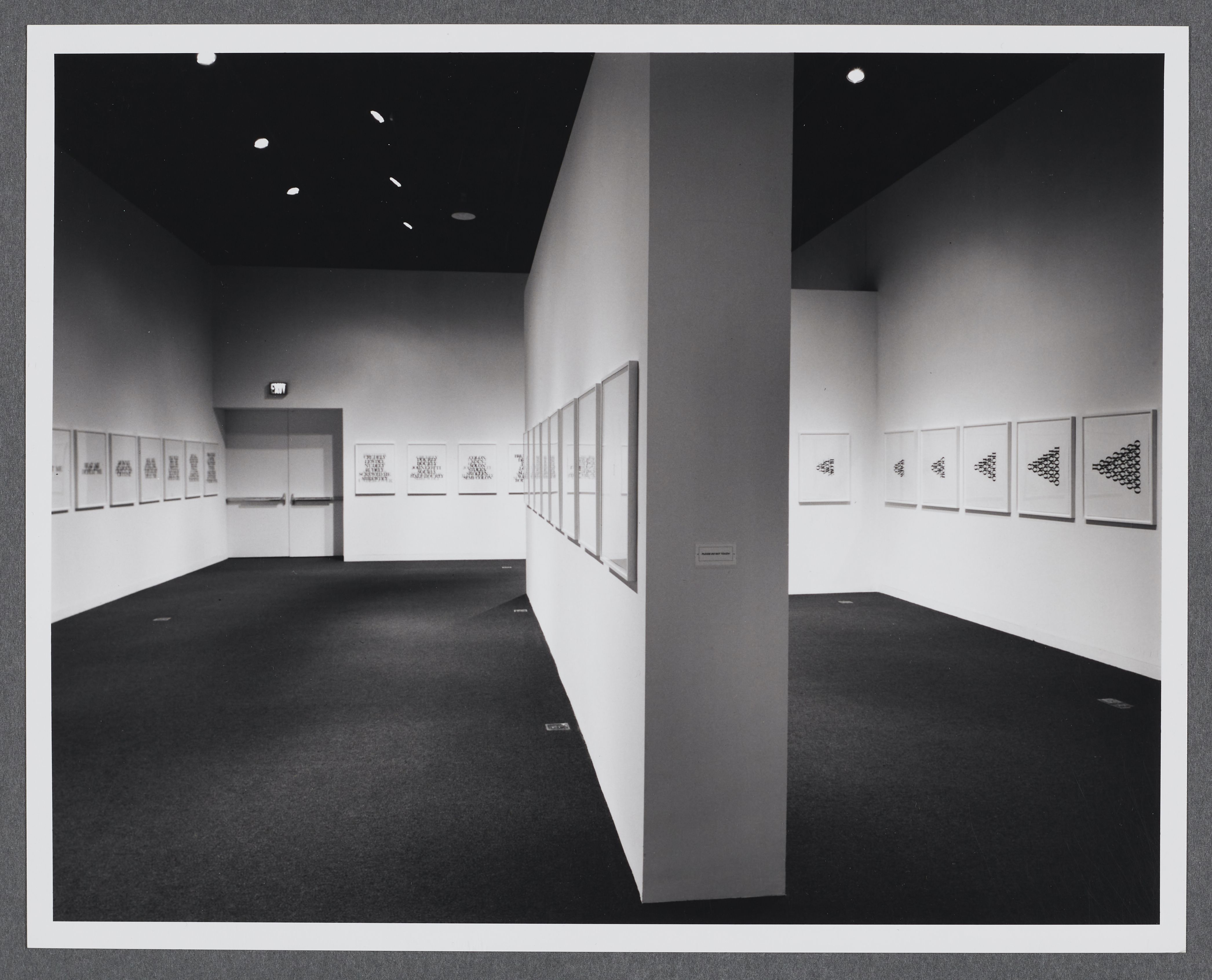 A gallery wall splits the room in half. Works of the same size are displayed in a row going across all of the gallery walls.