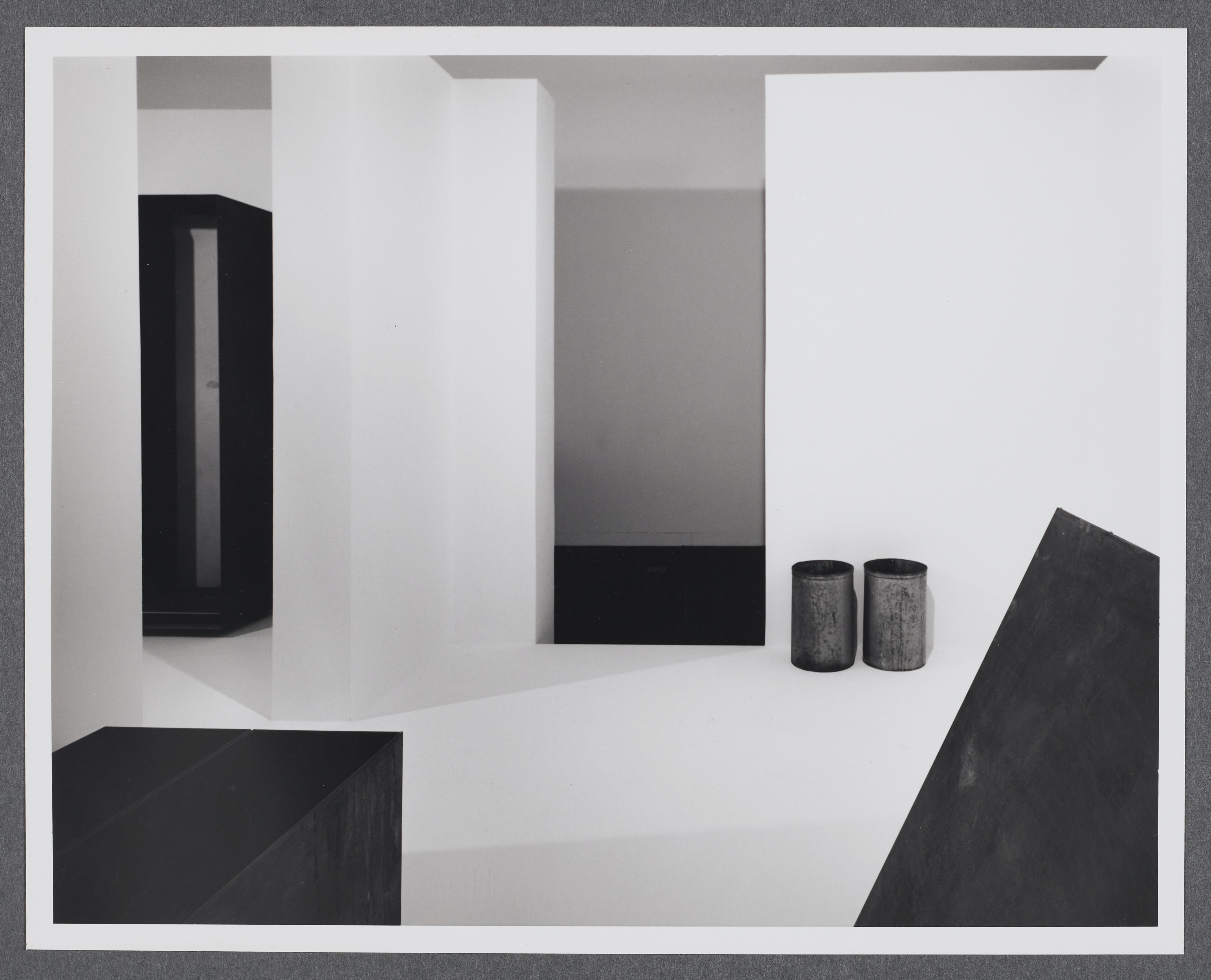 Steel sculptures are displayed in a wite room. Each are geometric forms such as rectangular prisms and cylinders.
