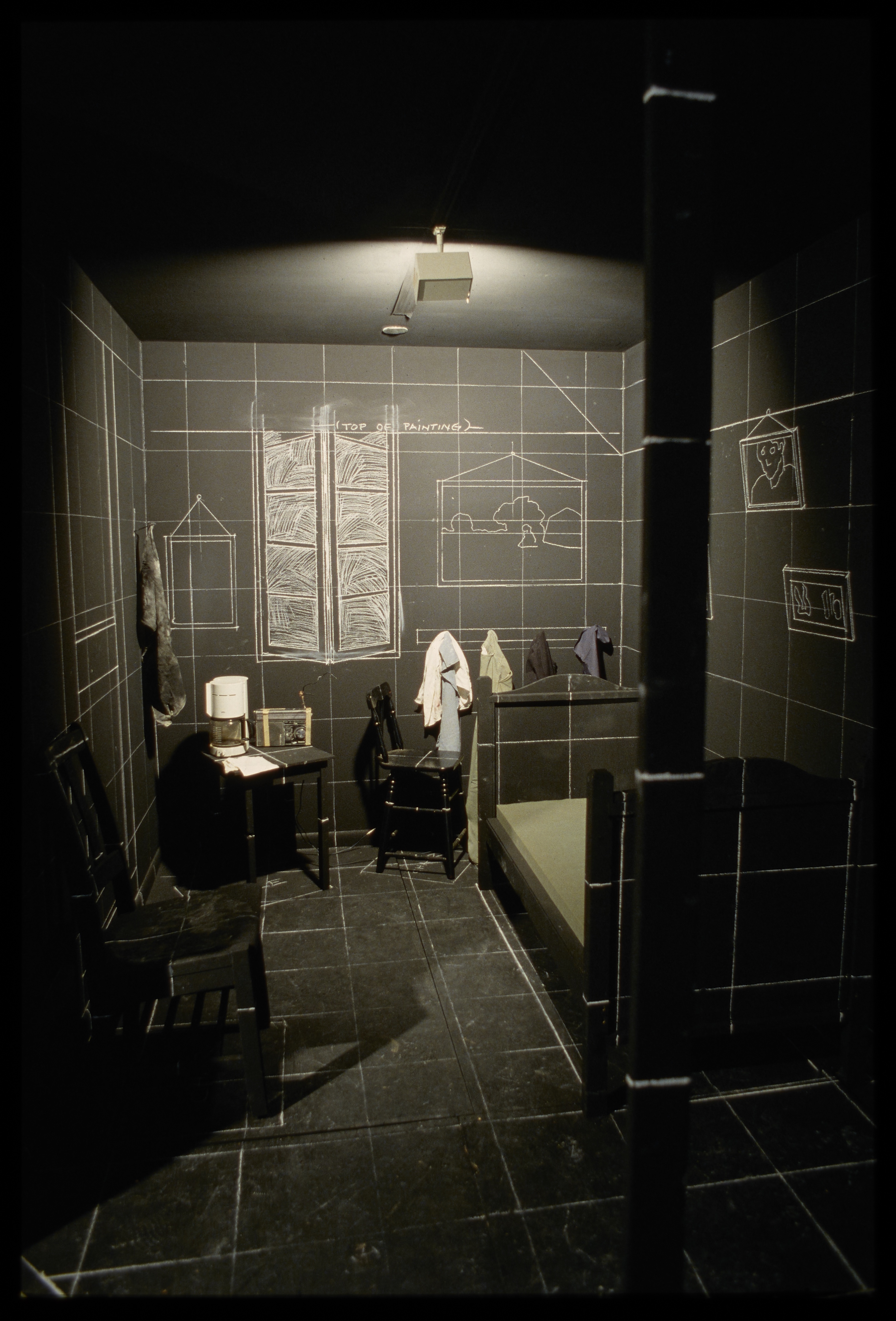 Black bedroom and furniture with chalk grid, chalk drawings of wall furnishings, and colorful clothes, mattress, and coffee maker.