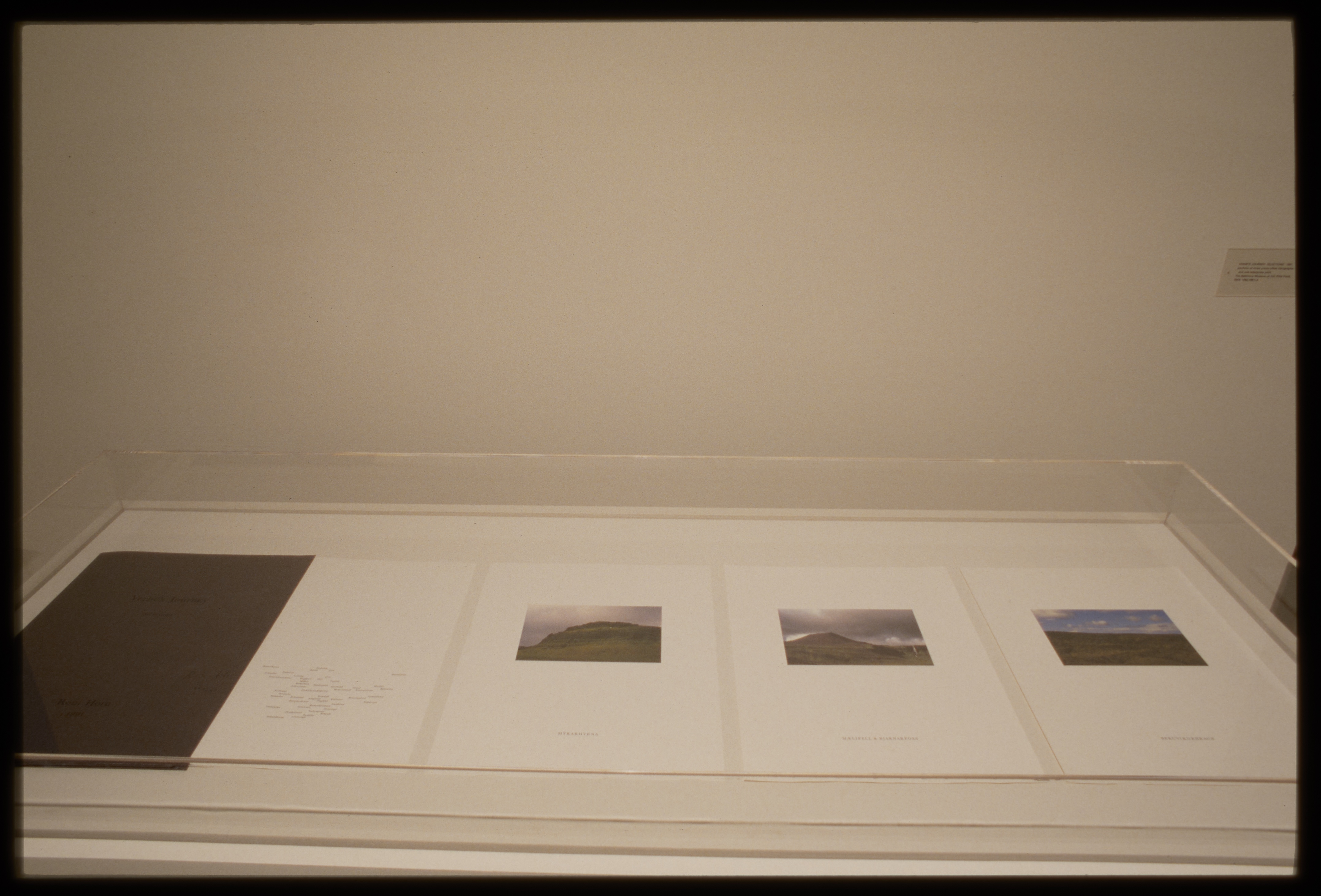Three landscape photographs of Iceland hills and sky on paper with text on right of book in glass case.