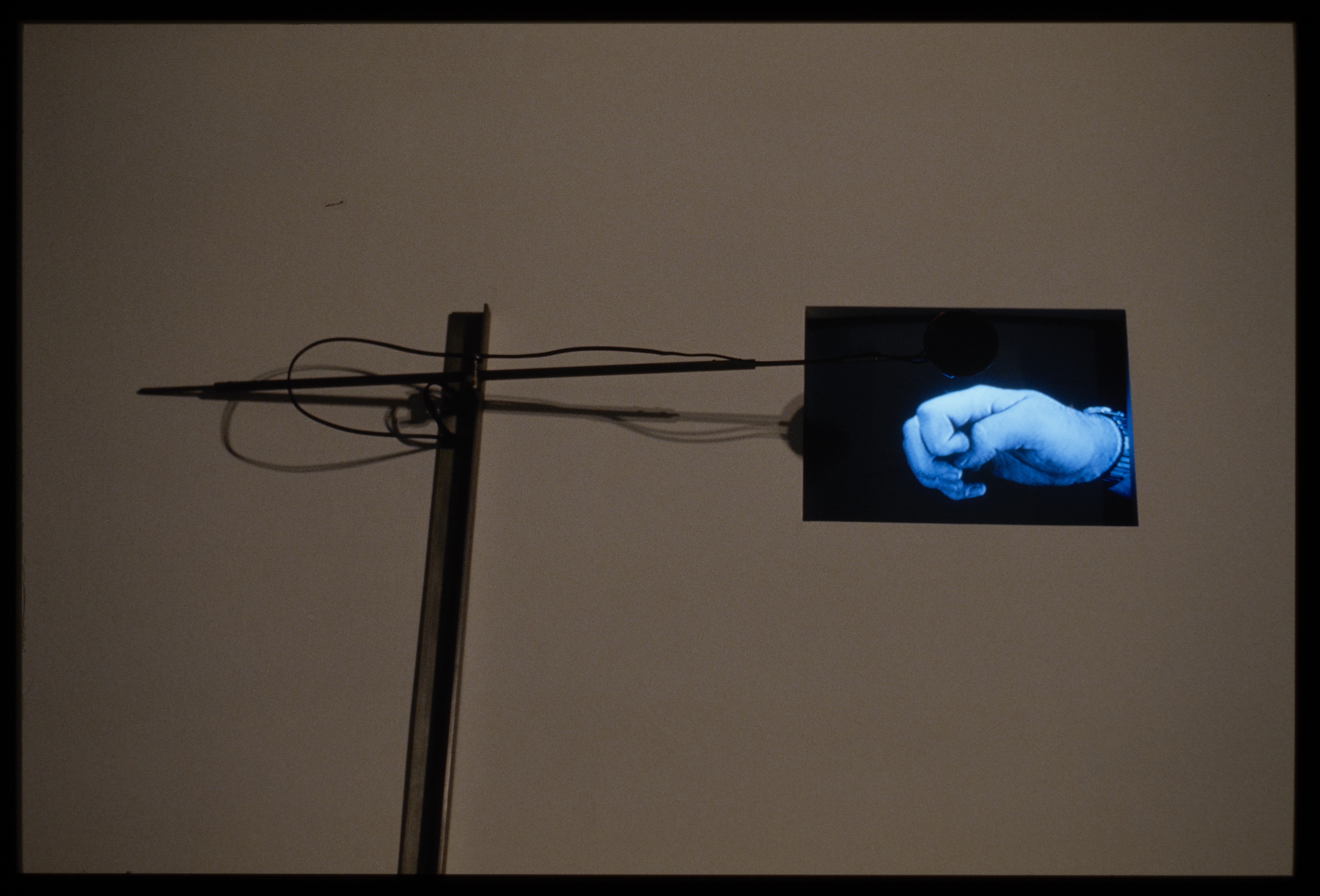 Art installation of metal and wired surveillance equipment connected to screen with close up of blue hand in shape of a flat fist.