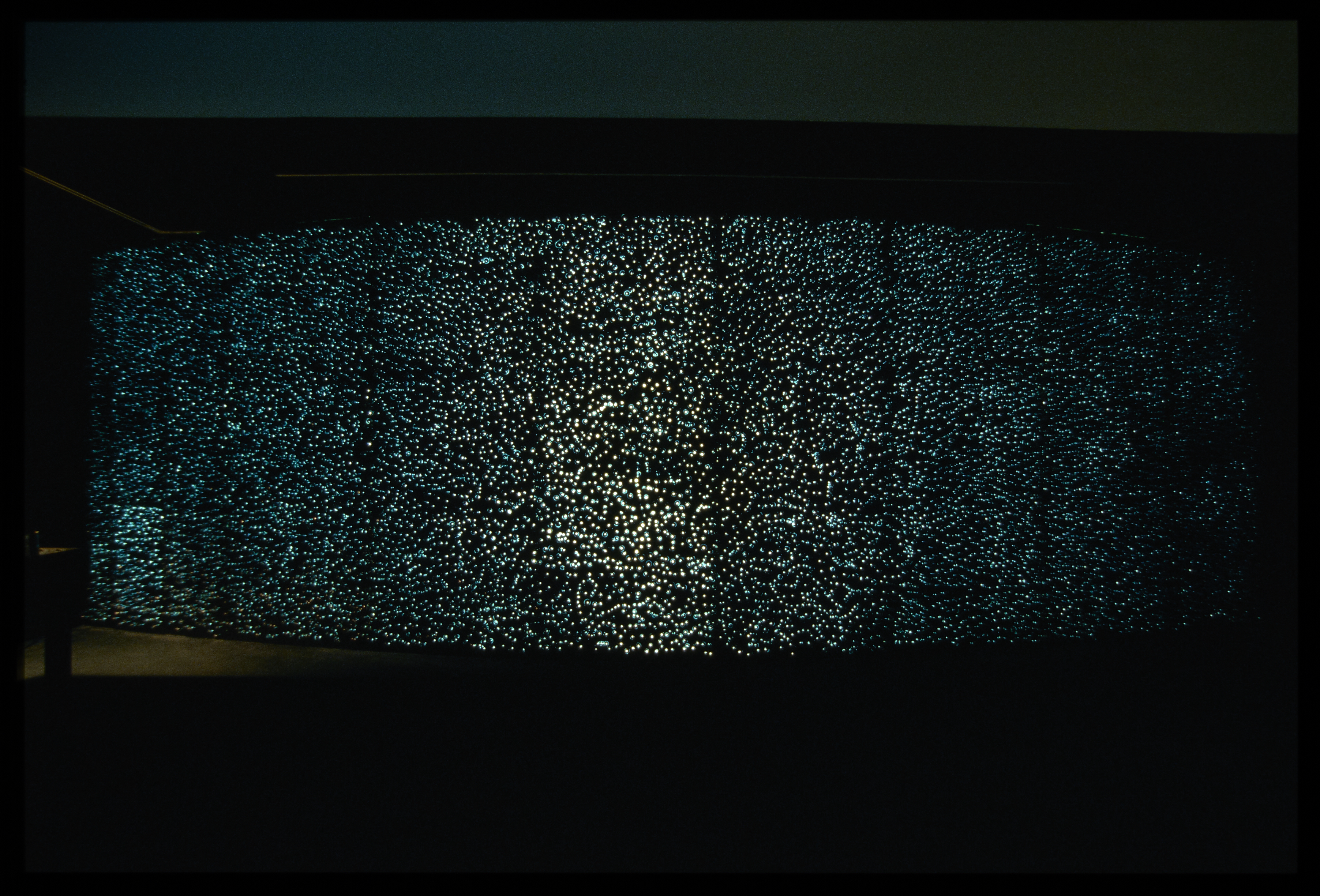 Panels of backlit glass bubbles create a large sparkling wall, bowing outward, in a dark space.