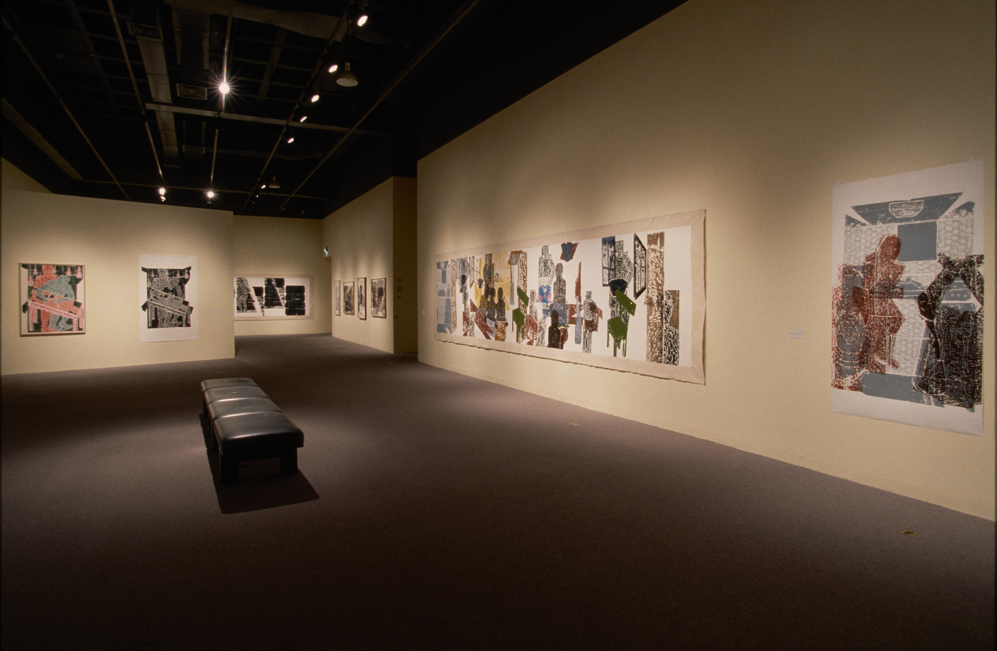 Large, muted-color woodblock prints hang on cream-color walls of a long gallery with a bench in the center for visitors
