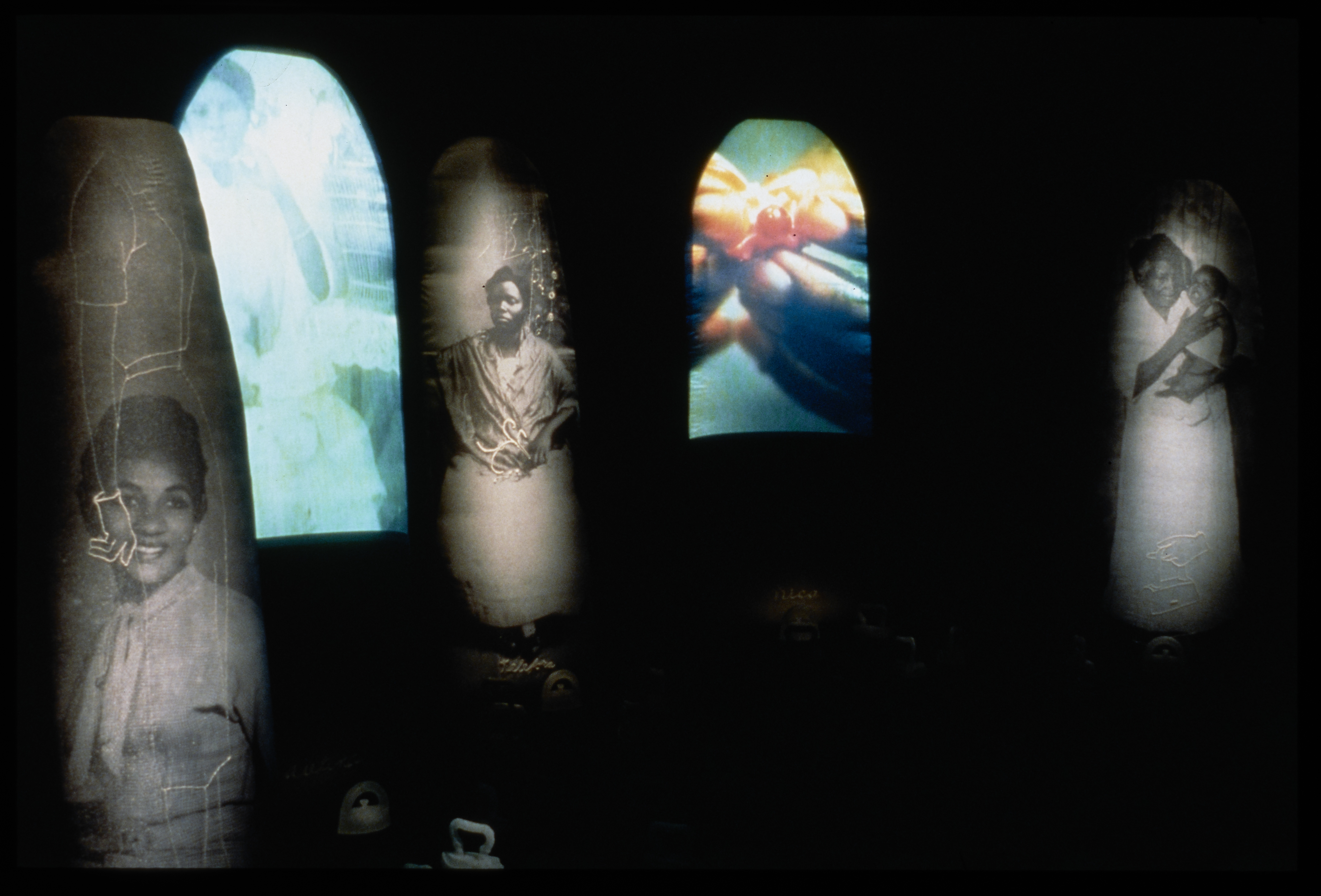 Color and black and white oblong strips of images of women, a woman and child and hands illuminate a black space.