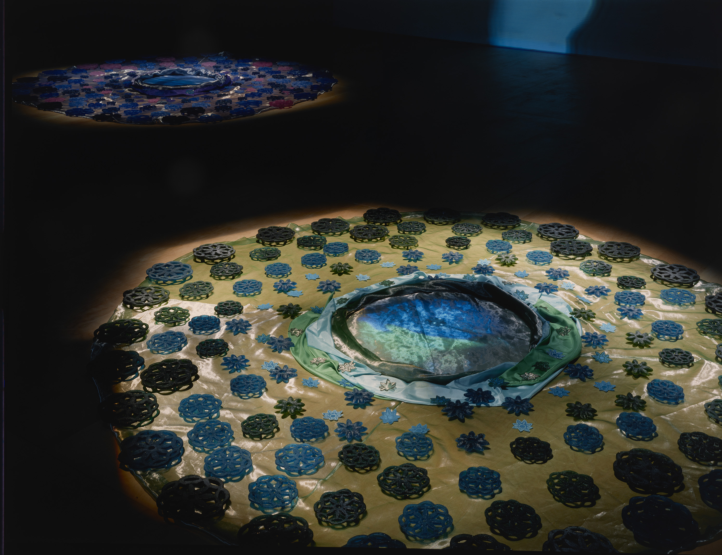 A group of large and small, blue and pink cast-glass flower shapes on pink-cream, shiny organza fabric