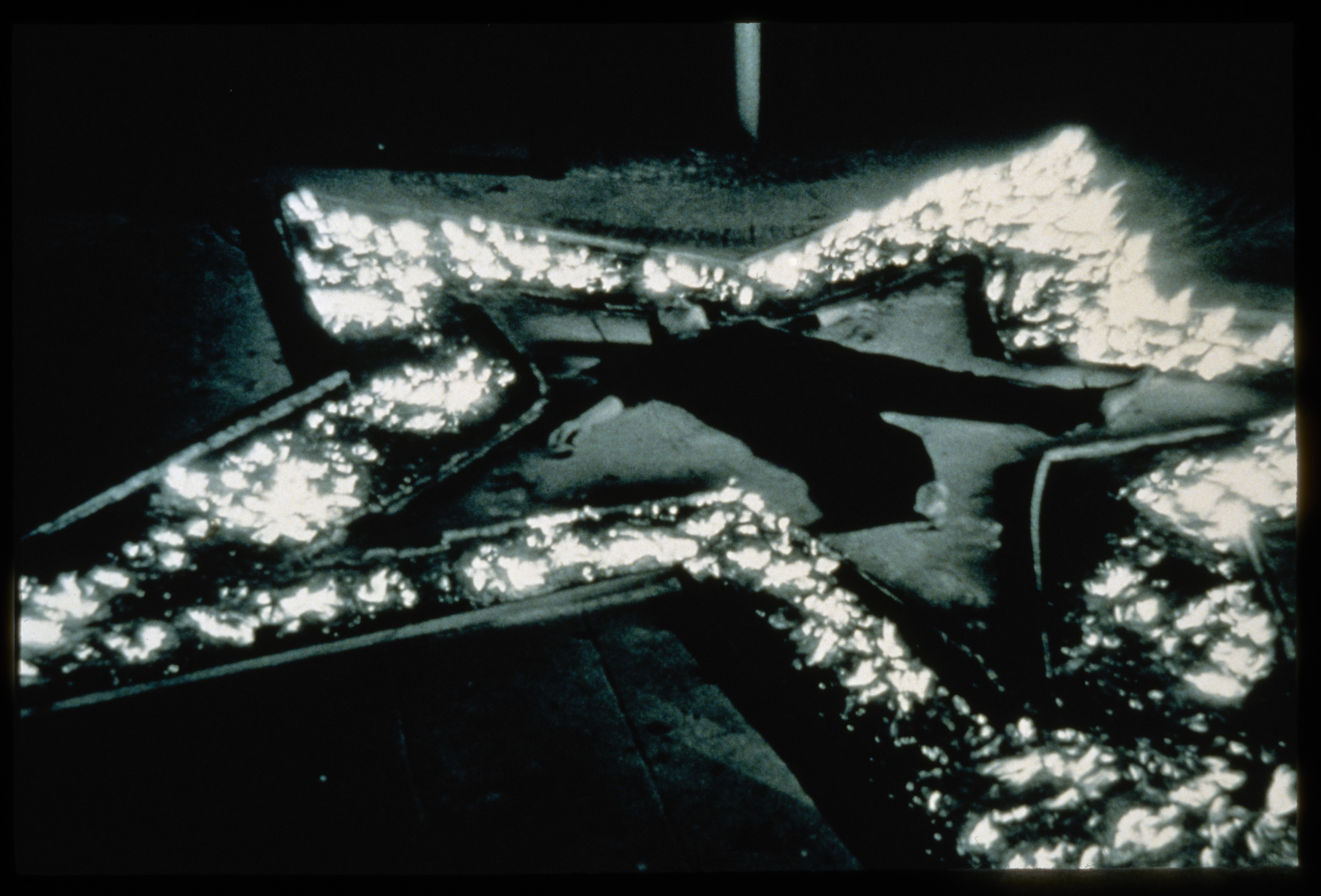 A monochrome image of a person lying face up, arms out, legs splayed, inside the brightly lit outline of a star on the ground.