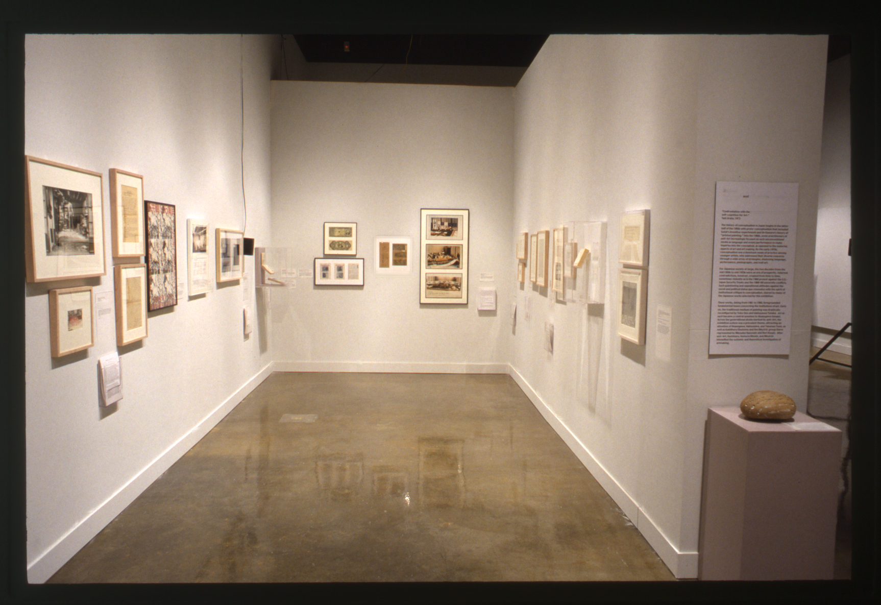 Corridor hung with multiple framed artworks on 3 walls. A sculpture sits on a pedestal in front.