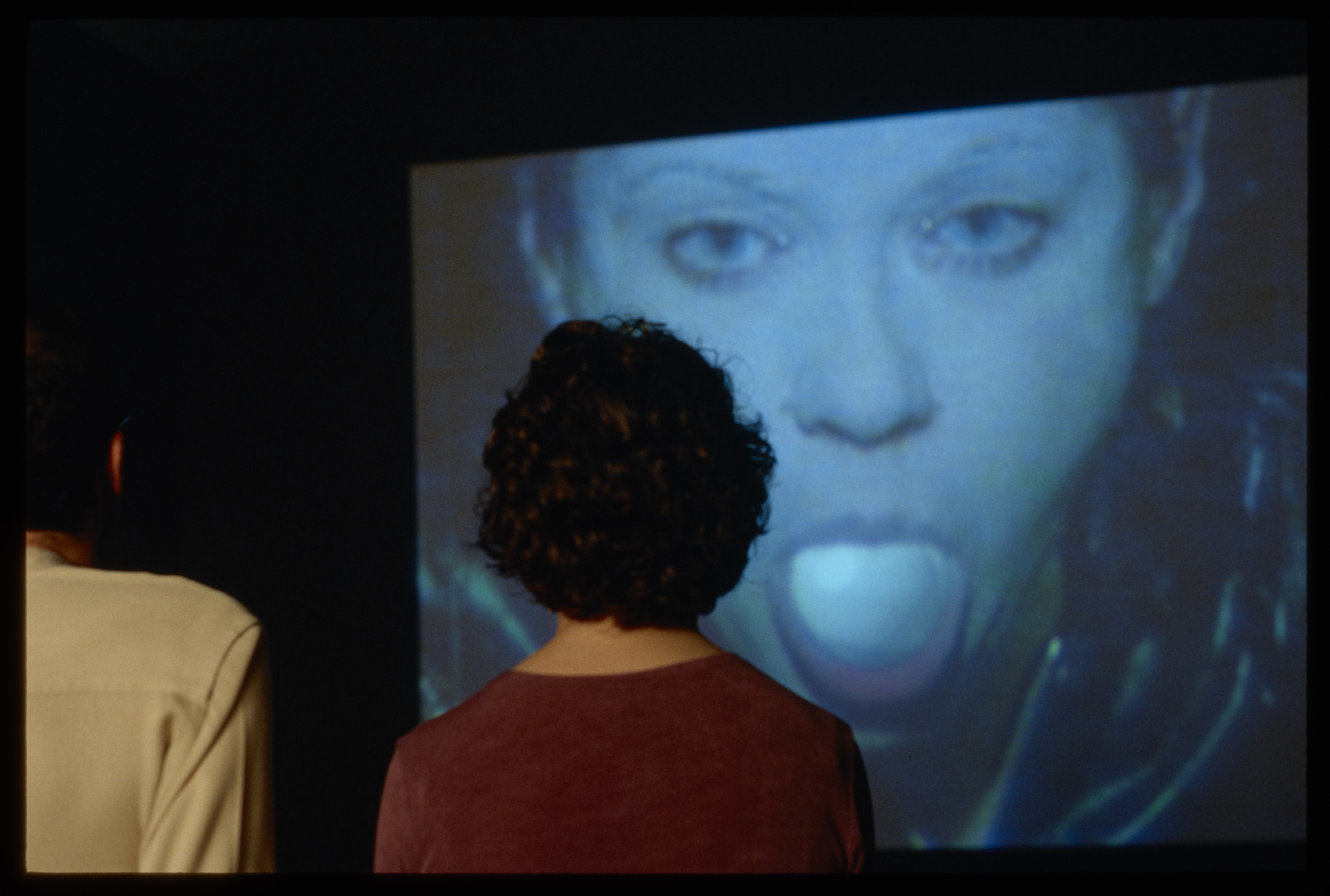 Two viewers watching a video with a young woman sticking out her tounge on the screen.