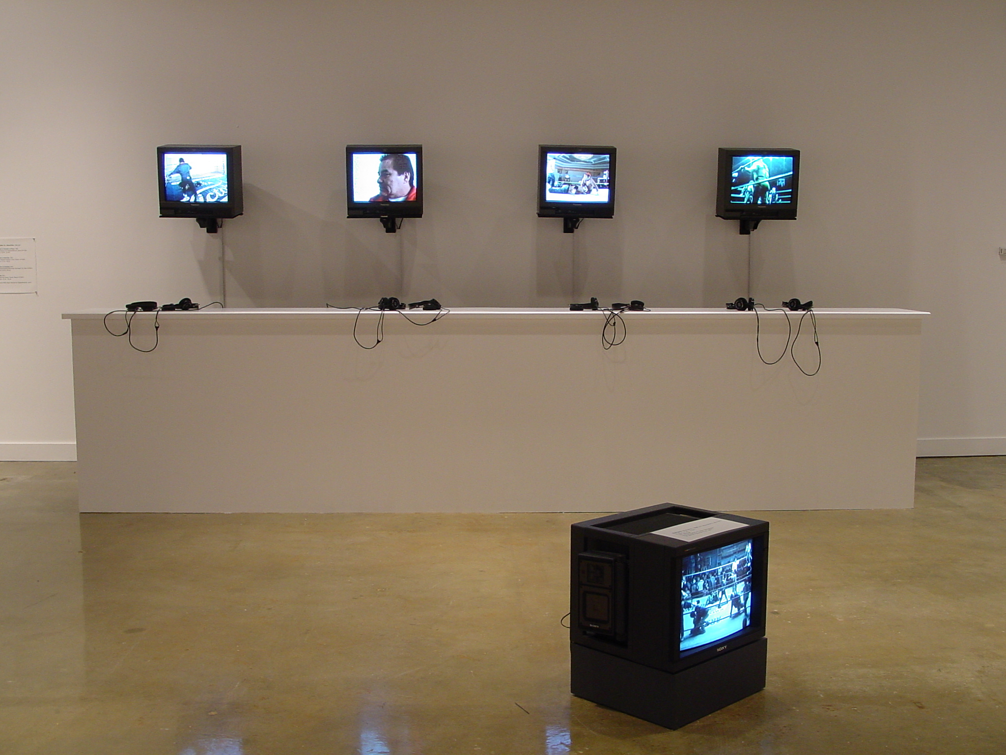 4 box monitors accompanied by headsets are mounted on the wall in a row. A 5th box monitor sits alone on the ground