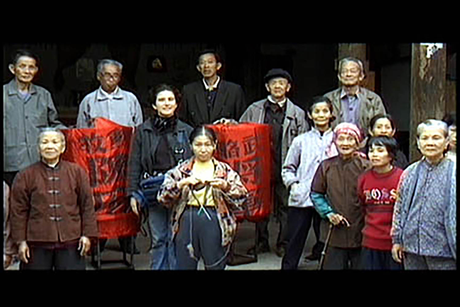 Captured in this video still, a collection of older men and women stare at the camera