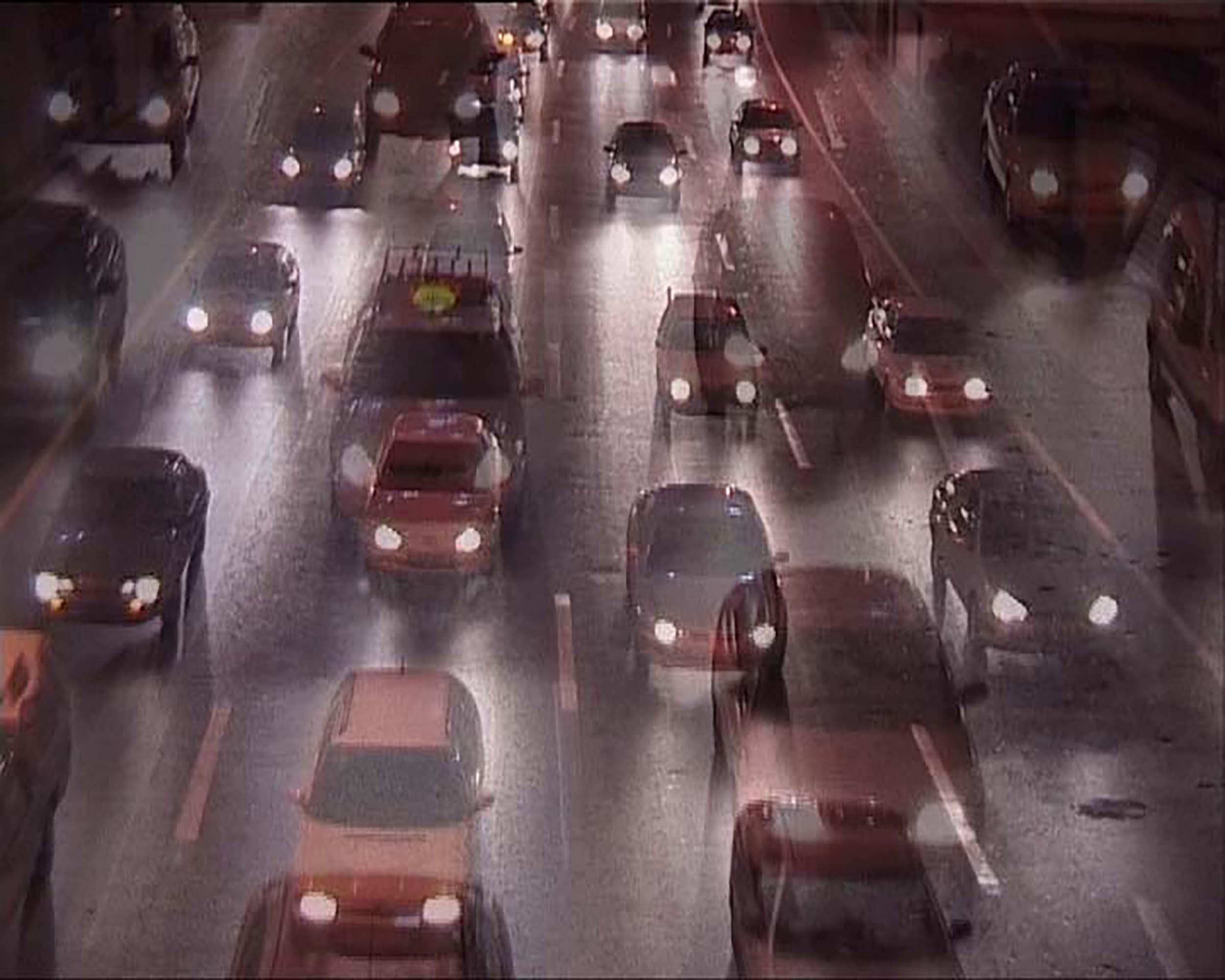 A video still depicting a traffic filled road, each car with headlights illuminating the night