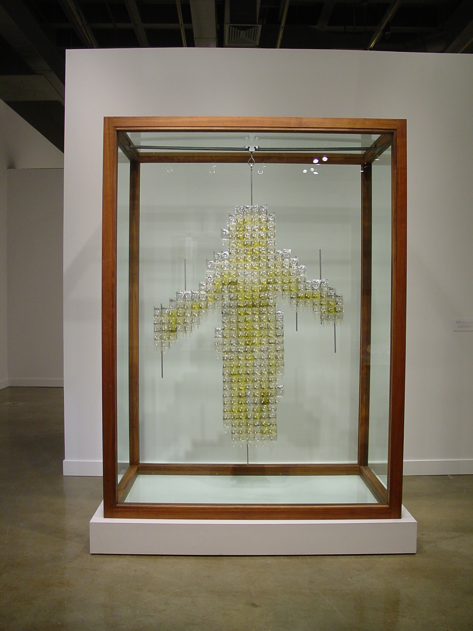 In a large walnut framed vitrine, various materials assemble into a hanging yellow figure with arms outstretched