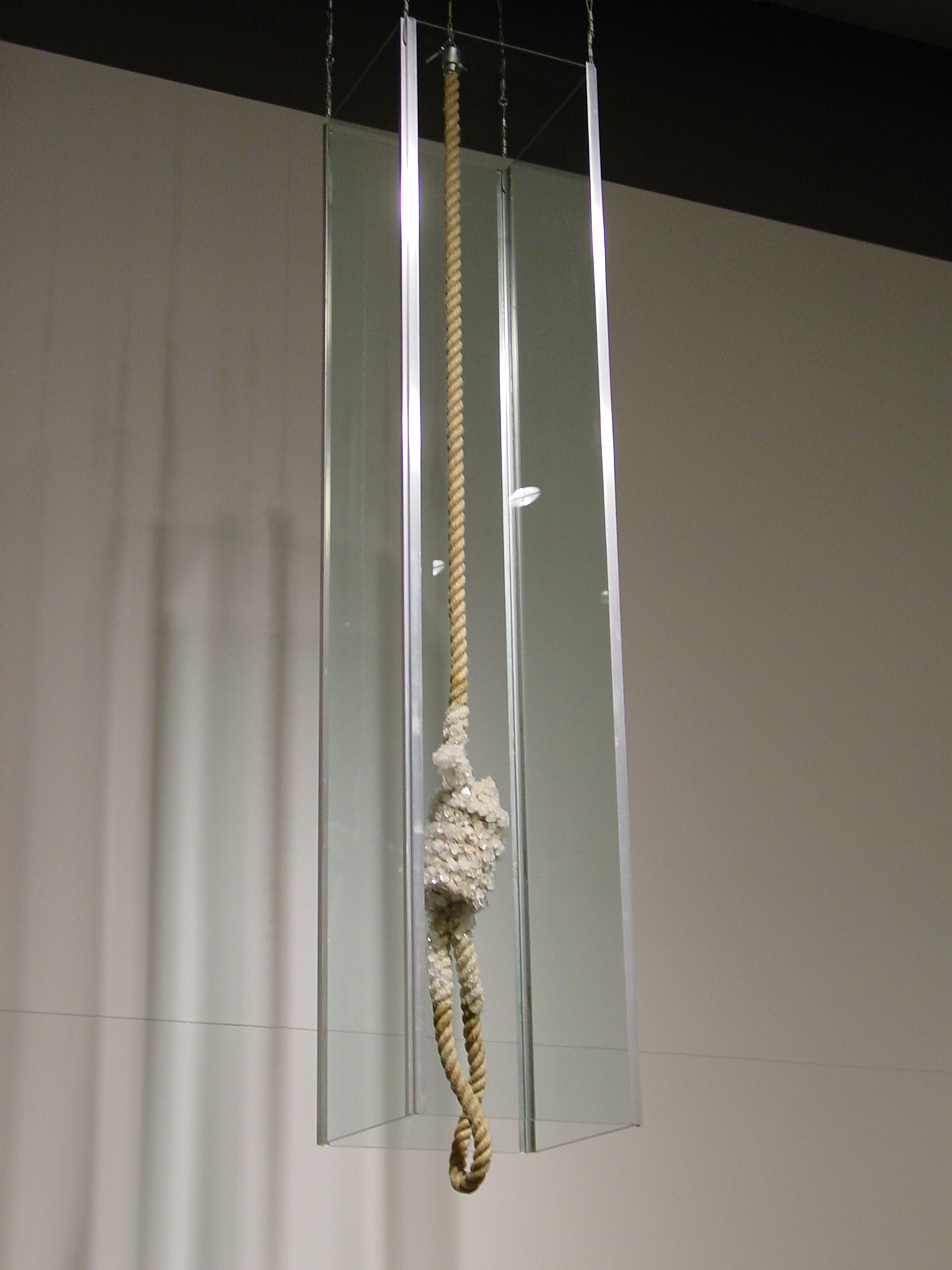 A noose hangs, suspended from the ceiling, partially covered in crystals and surrounded by a clear case