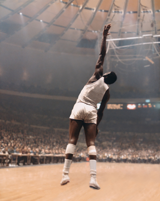 Manipulated photograph of a filled basketball arena and a single player, jumping with one hand up to block a shot