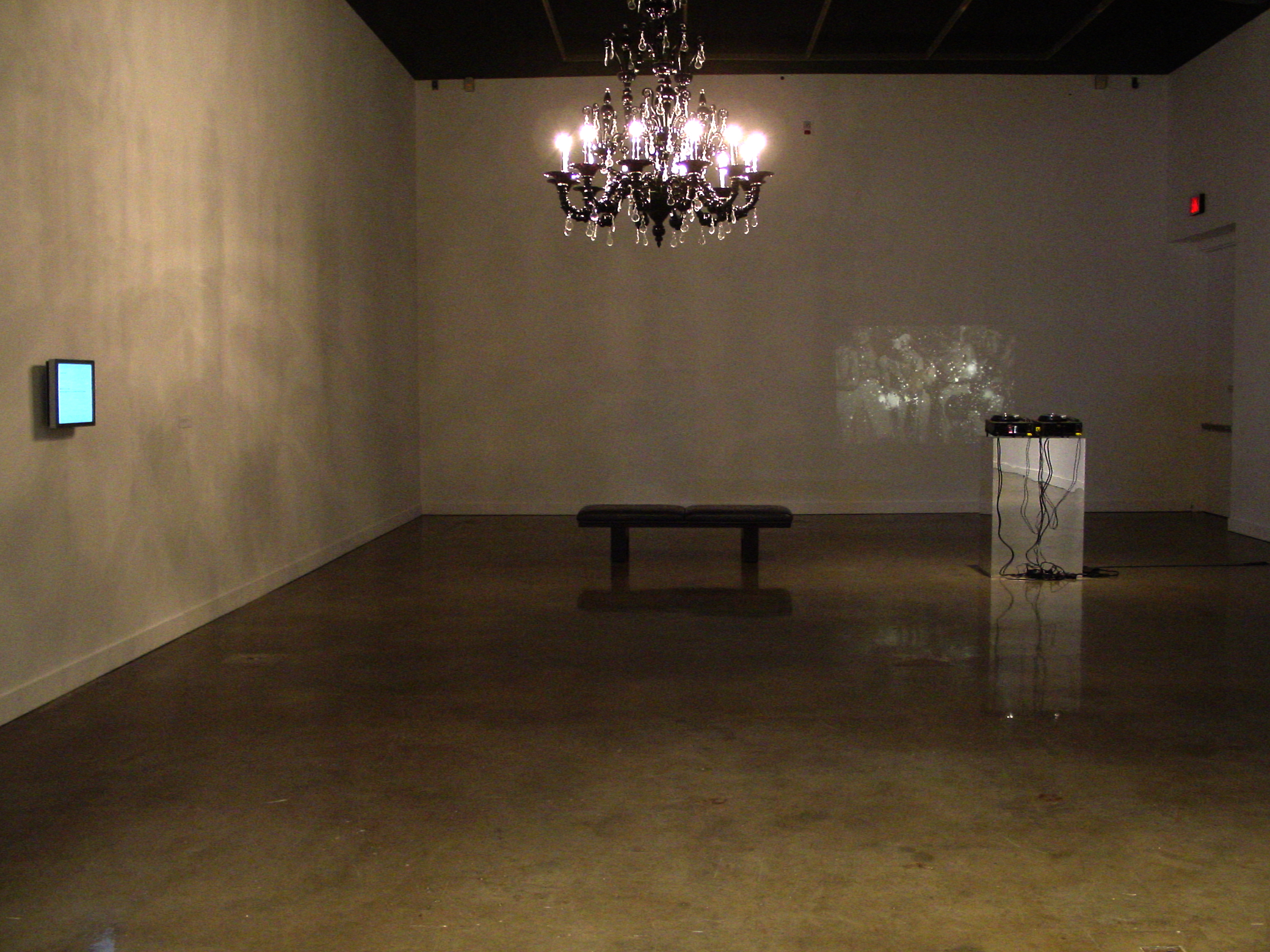 View of a large mirrored sculpture reflecting the gallery upside down and 3 scholar’s rocks on pedestals under glass cases.