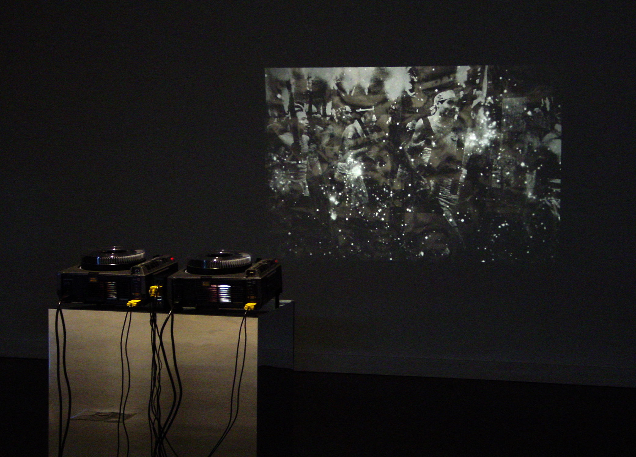 Two slide film projectors side by side on a mirrored pedestal projecting an abstract black and white image on a wall.