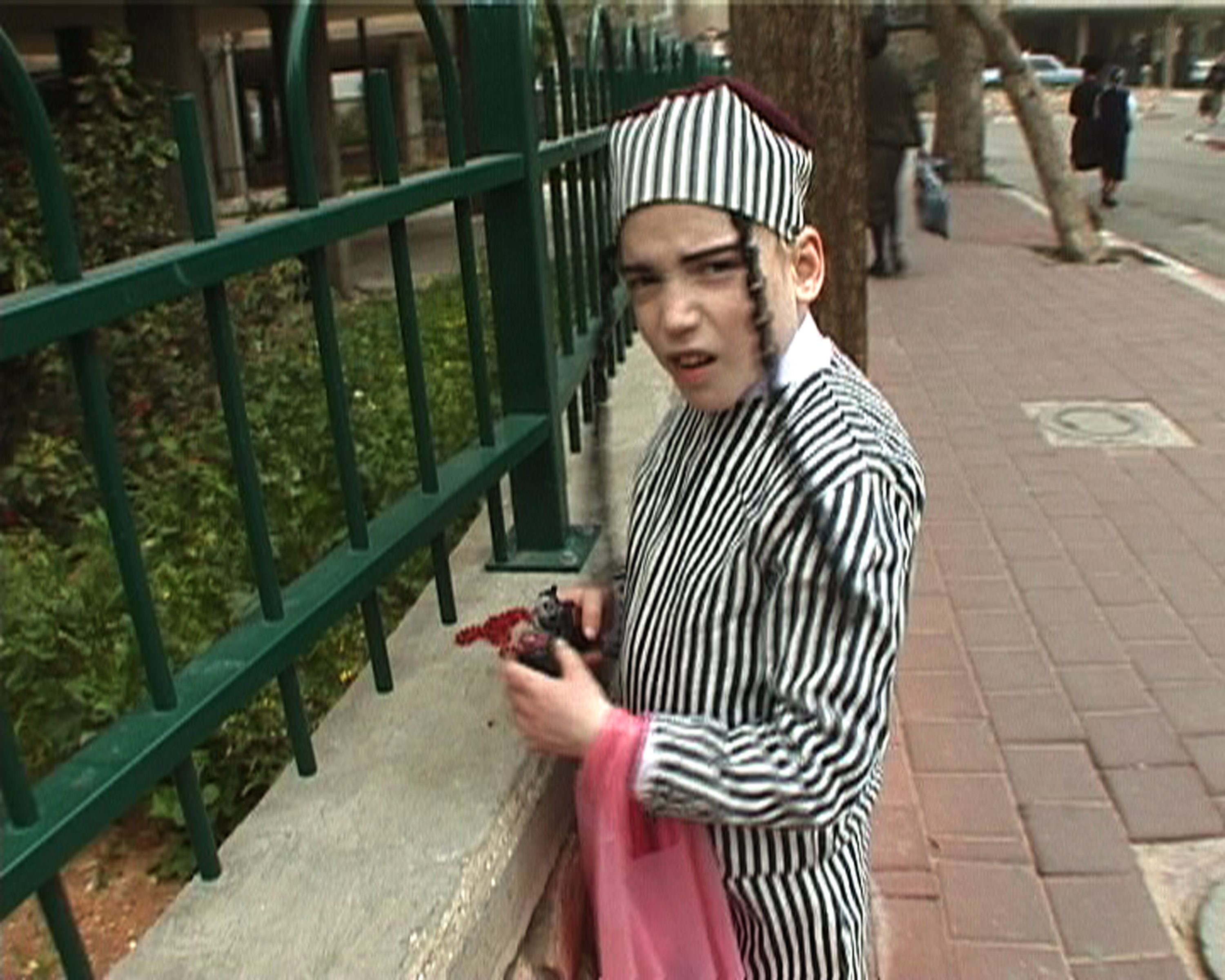 A child dressed in a striped black and white costume and matching hat holding a toy cap pistol looks surprised at the camera.
