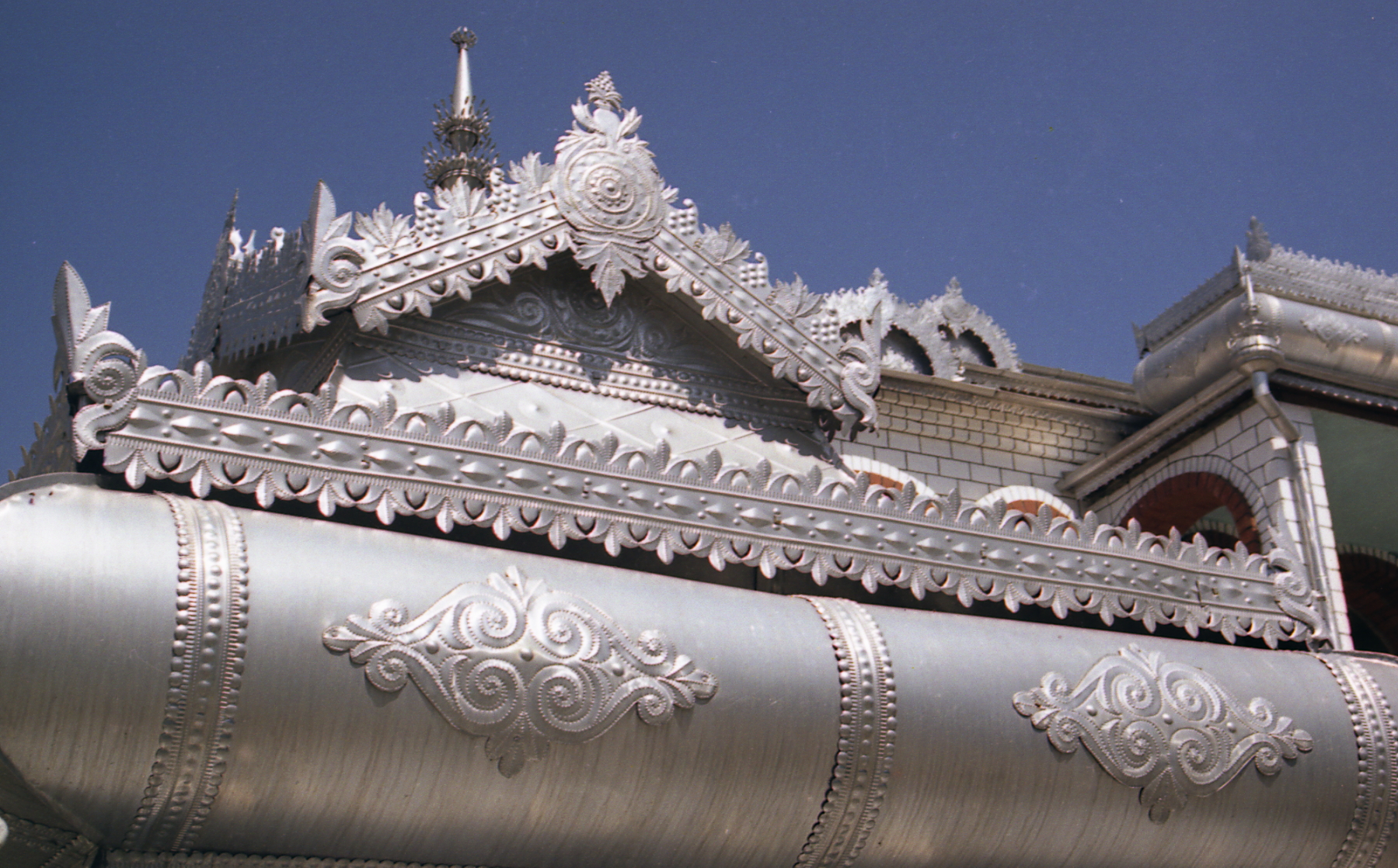 Video still showing an ornamental rooftop painted silver with a blue sky background.