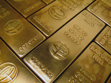 A close view of small shiny sculptures made to look like bars of gold are arranged on the floor in a brickwork pattern.