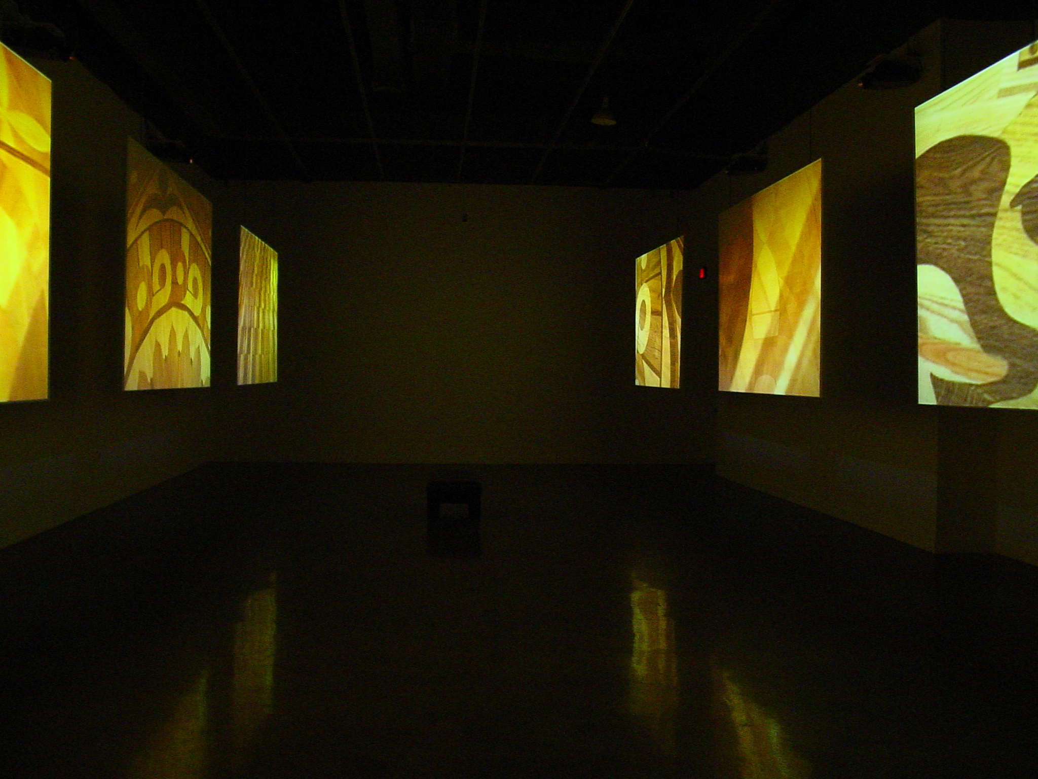 A darkened room with six video projection screens hung from the ceiling showing detail images all golden and brown in color.
