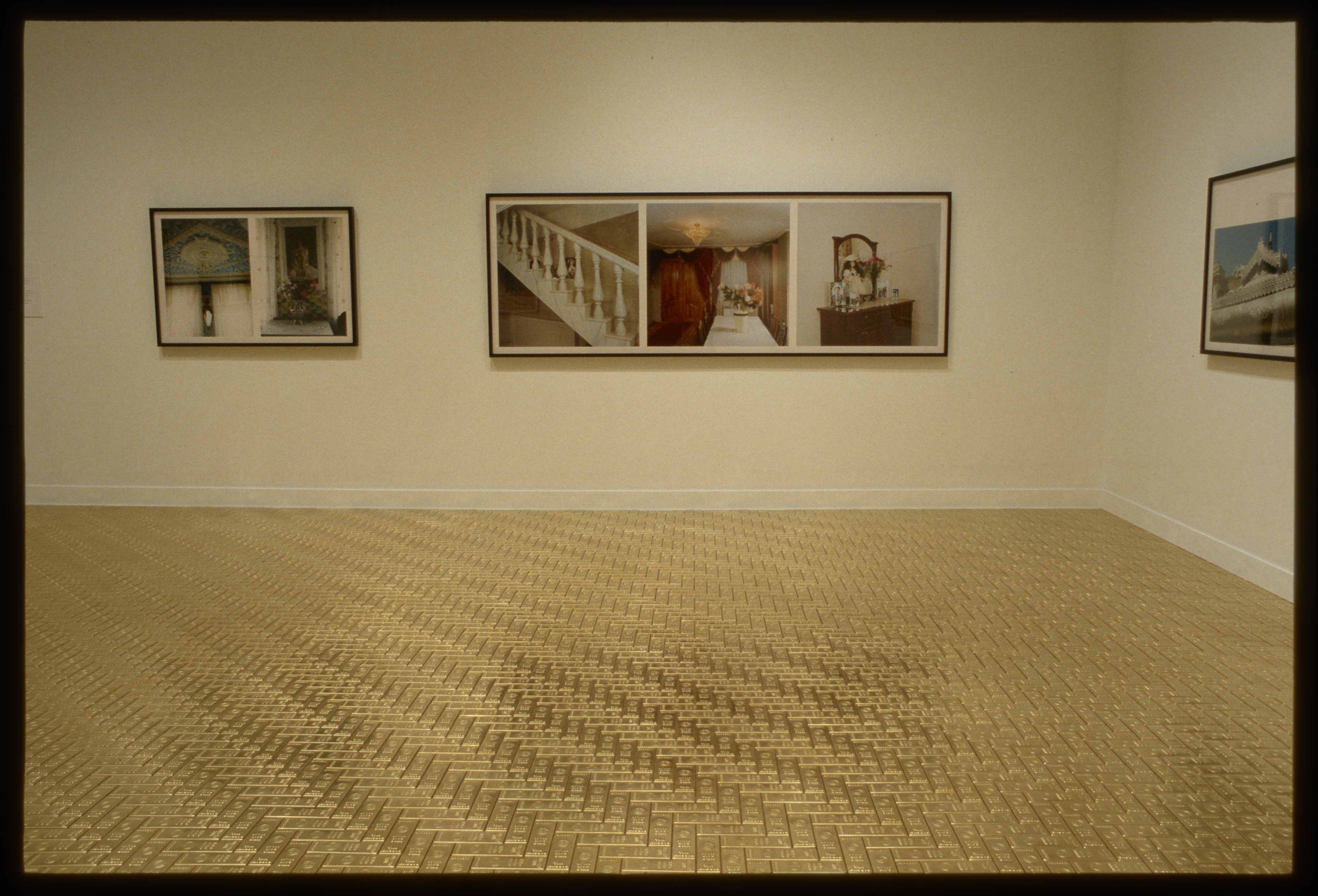 Large framed colorful photographs hung on two walls in a room with a shiny golden floor.