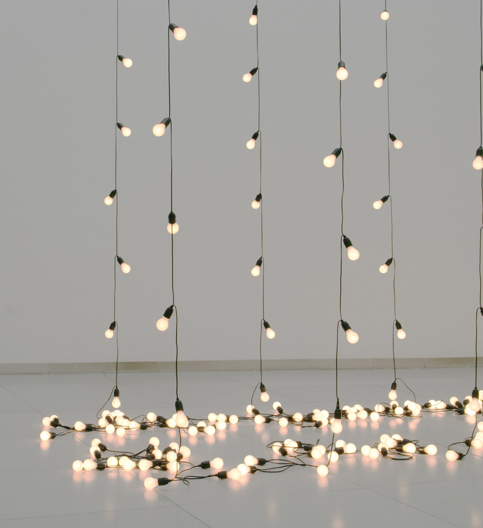 Six strands of small white light bulbs hang down and lie together on the gallery floor.