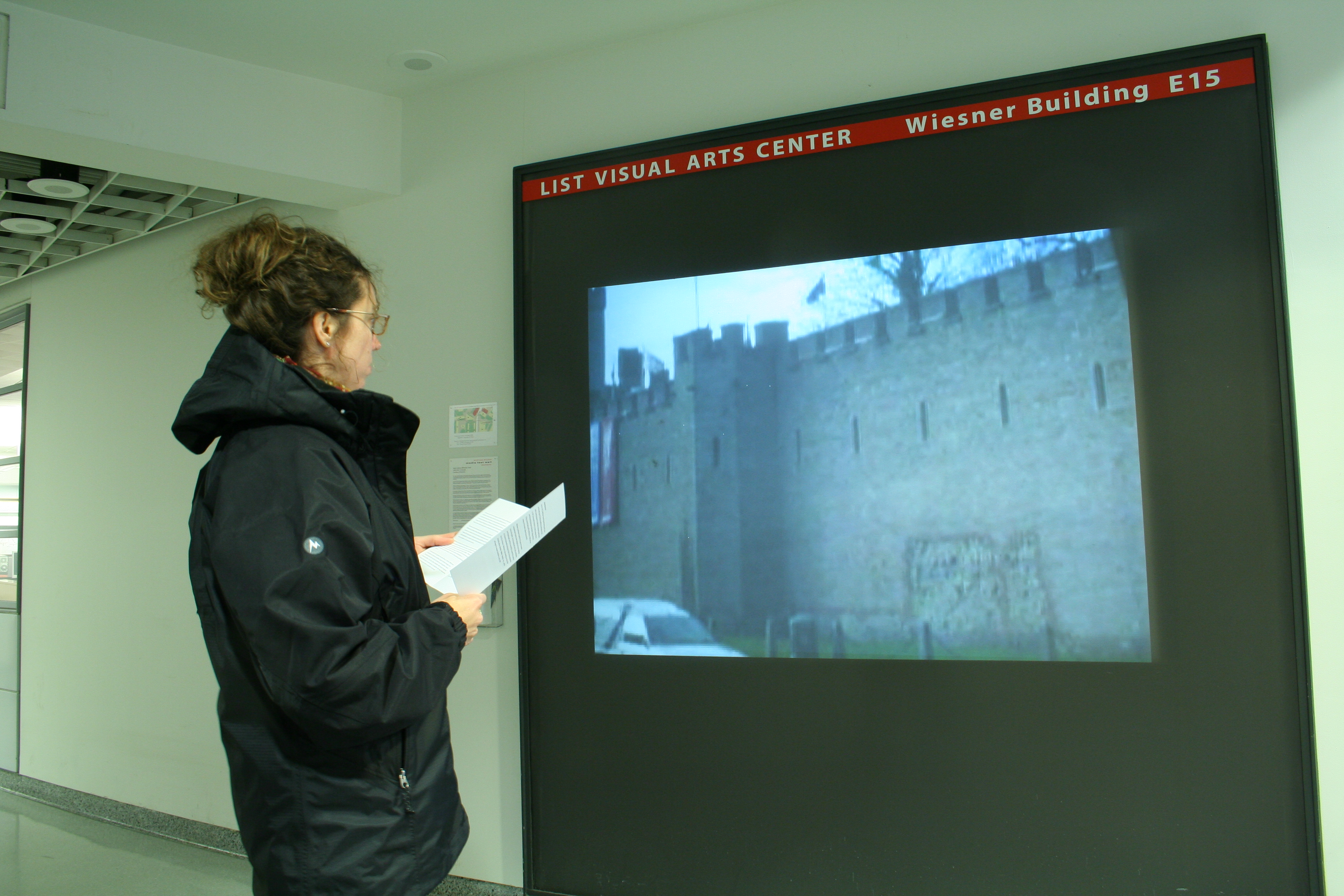 A visitor stands in front of video projection in a hallway showing a structure that has walls like a castle.