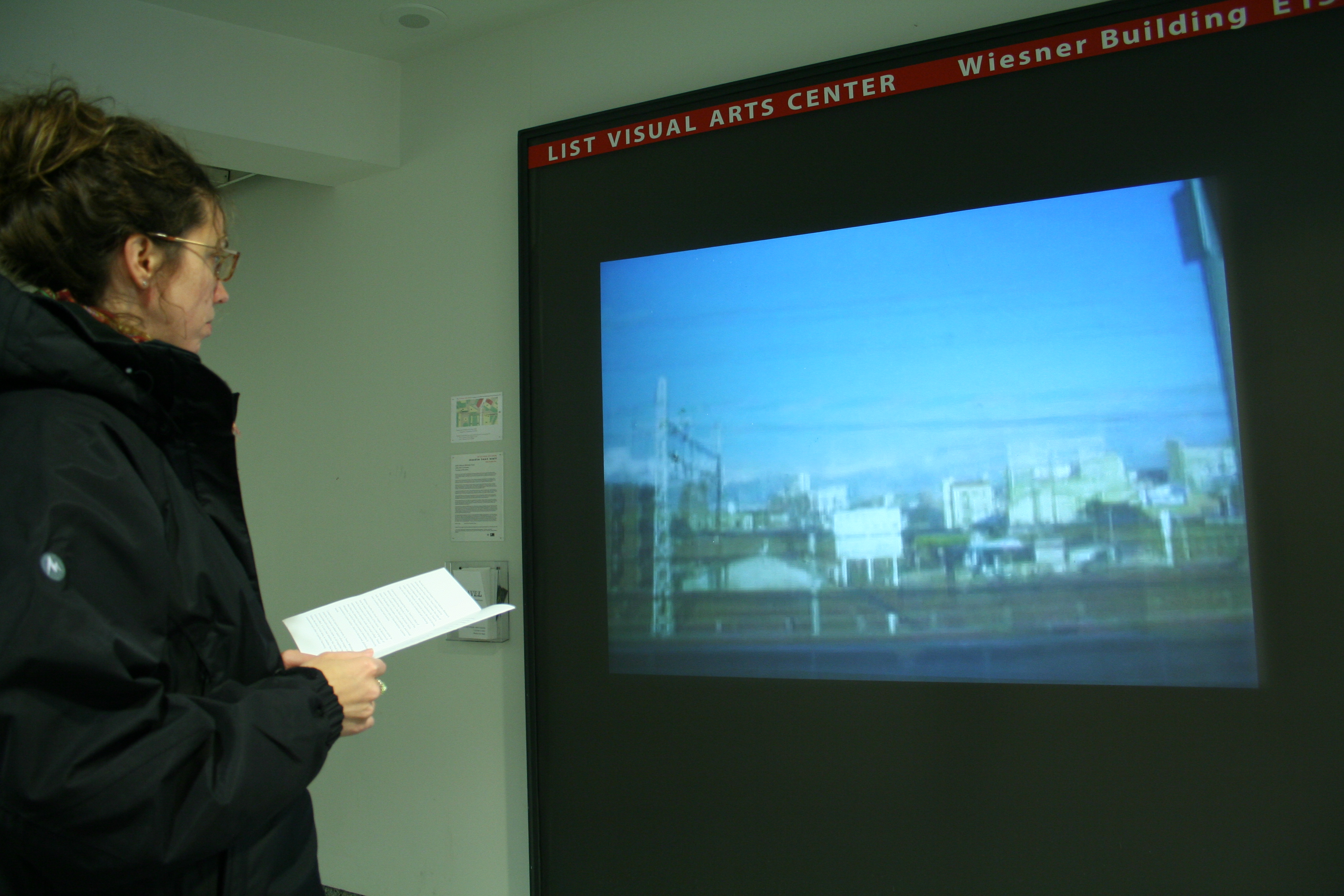A visitor stands in front of video projection in a hallway showing a blurry view of a city scene with buildings.