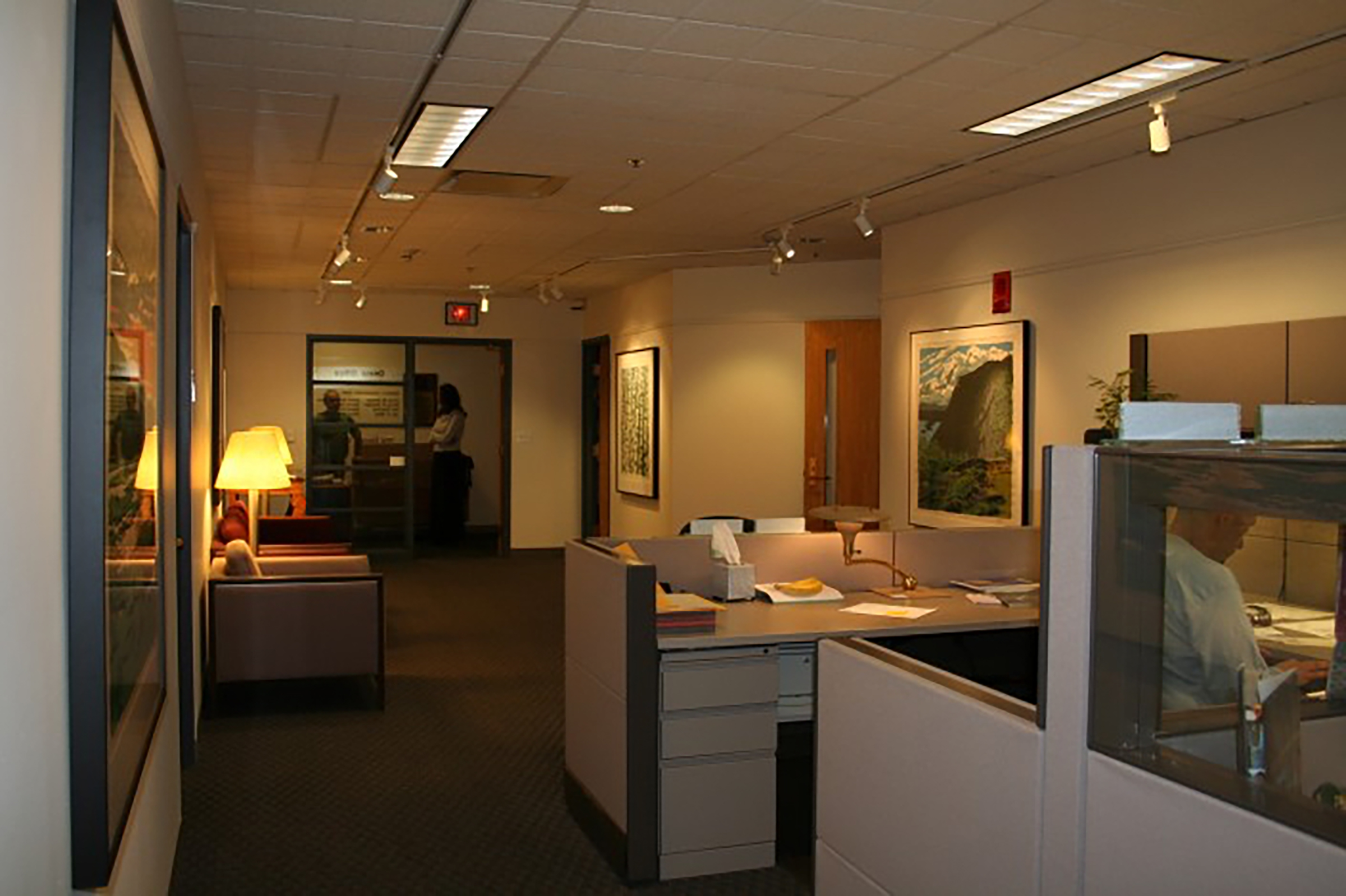 A rocky mountainside sits in the foreground with a large green mountain in the background. The sun sets as clouds roll in.
