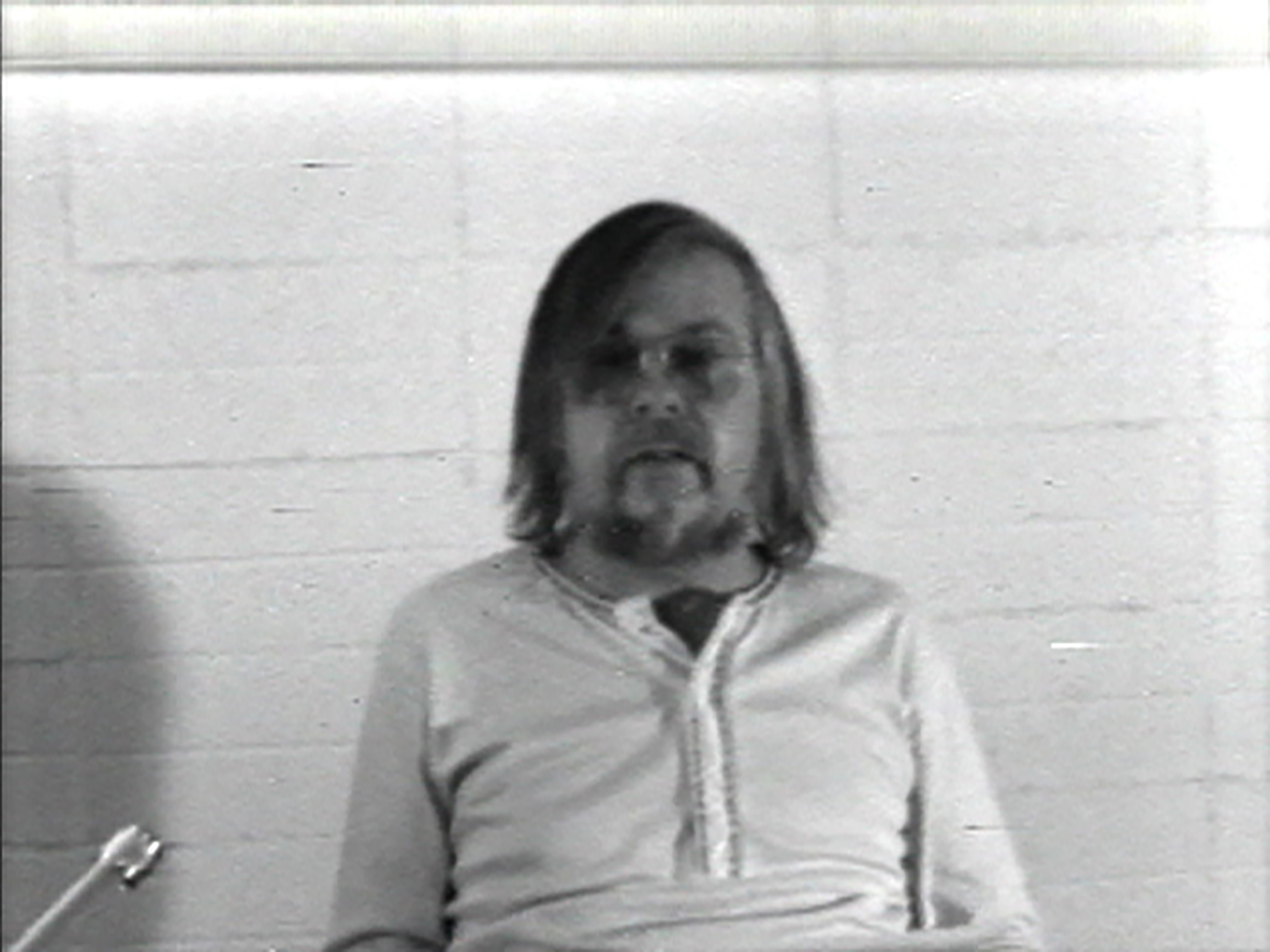 Man sitting in front of a cement wall with a microphone in the front left corner.