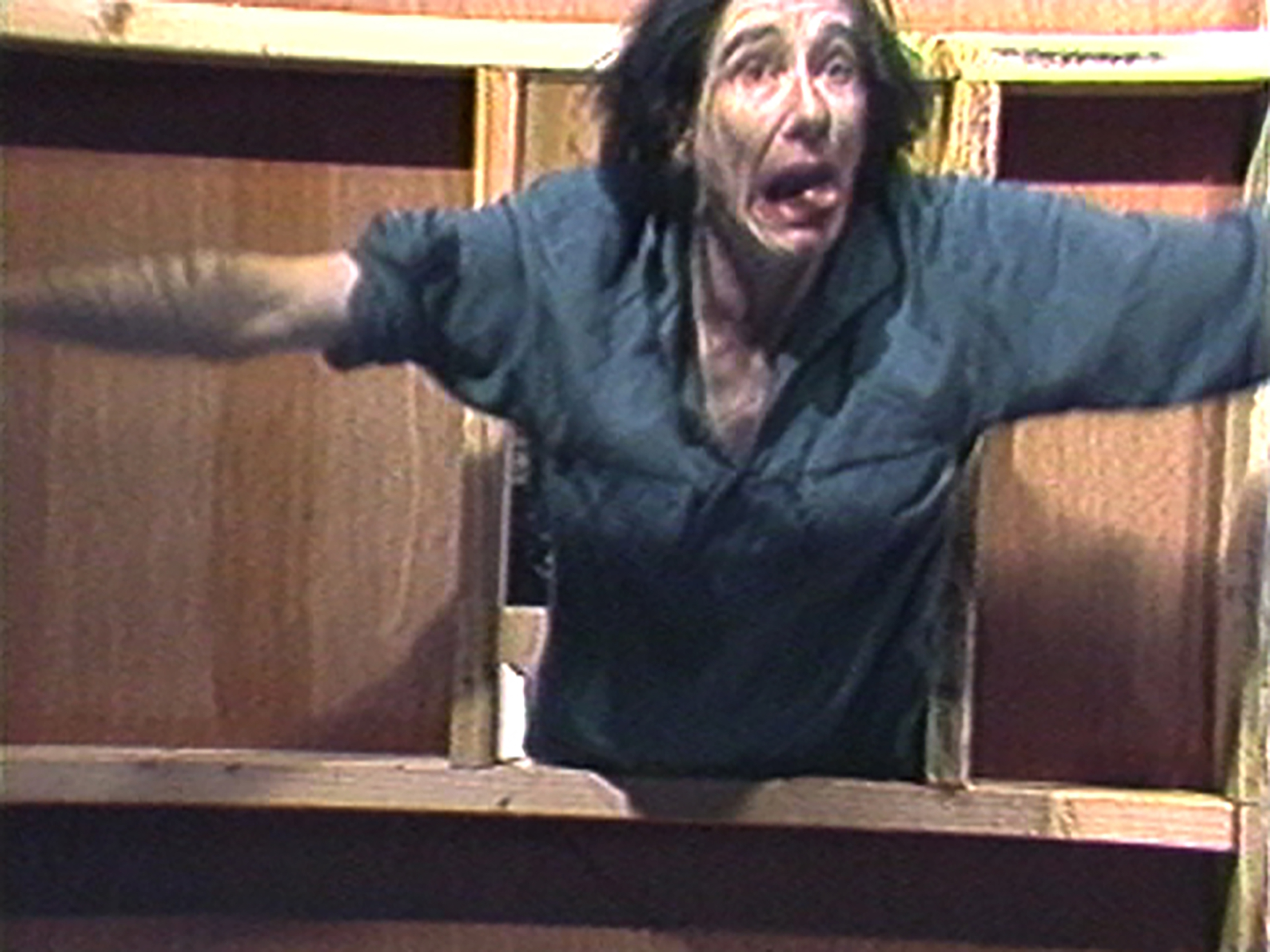 Grainy still of a person appearing to jump through a stage prop window.