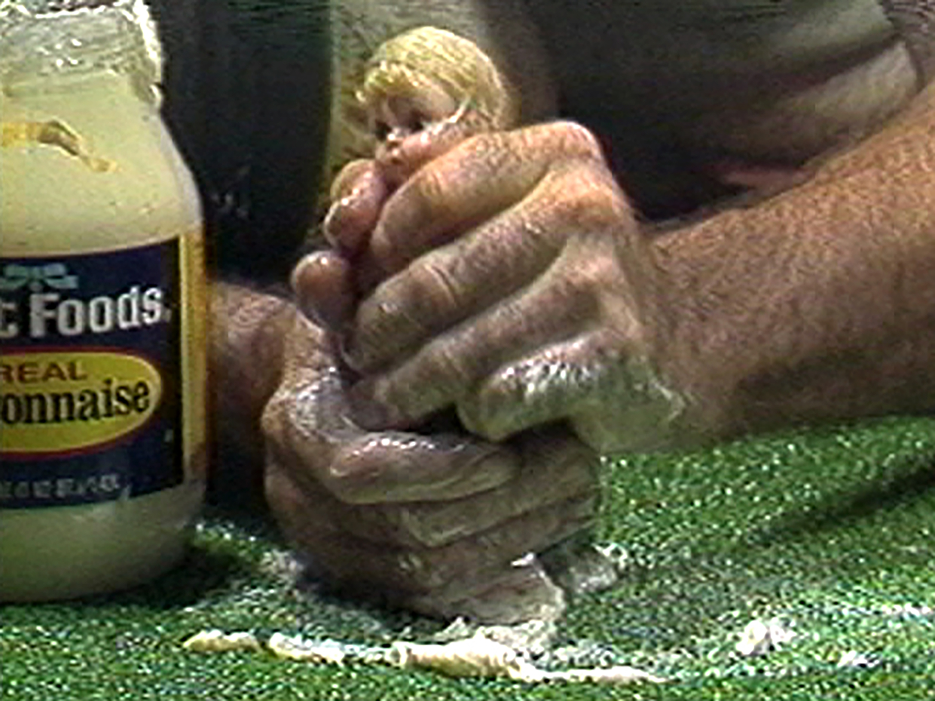 Close view of hands squeezing a small doll with mayonaise.