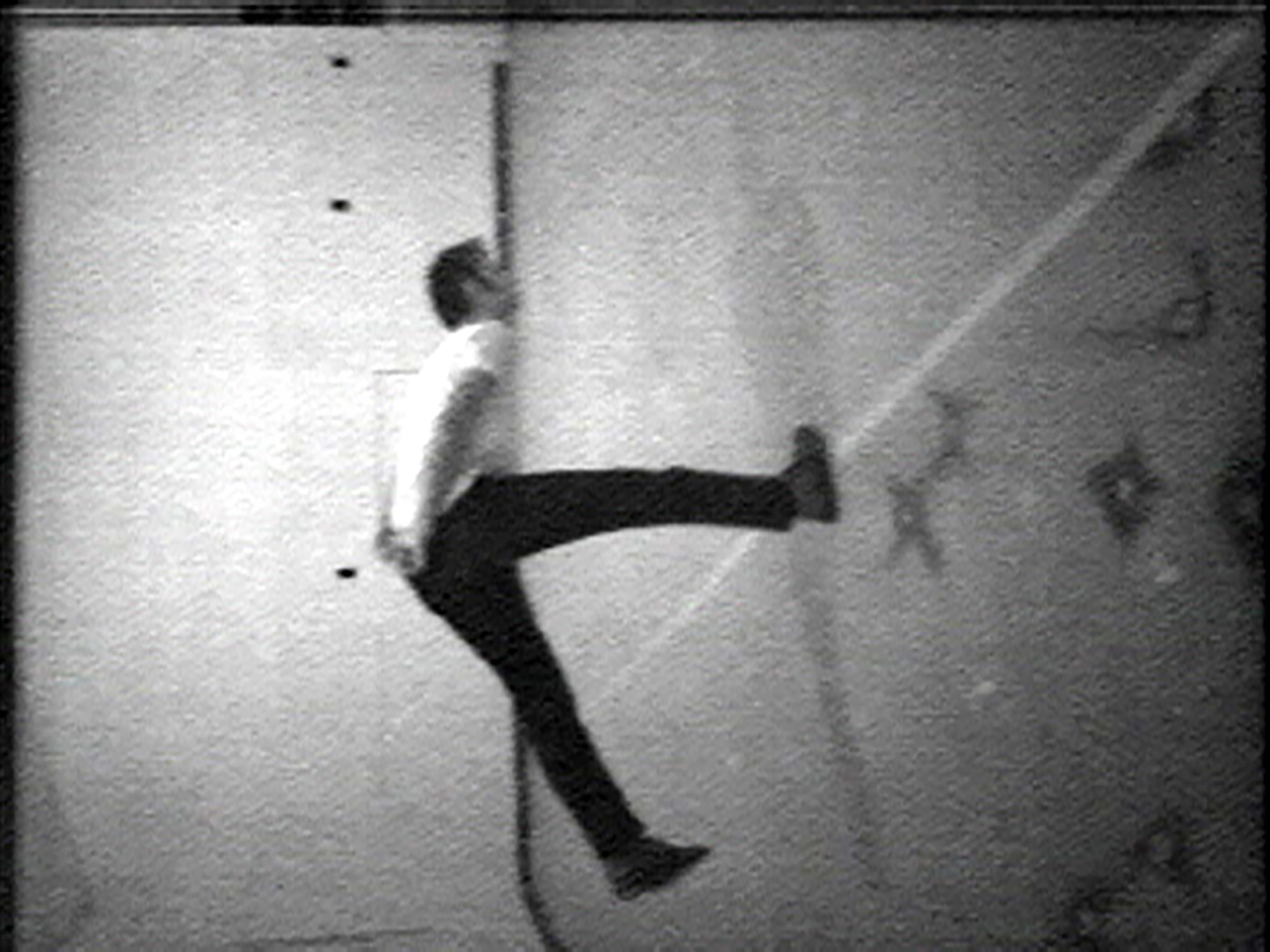 Black and white image of a man standing on one leg with his body slanted forward in a T shape.