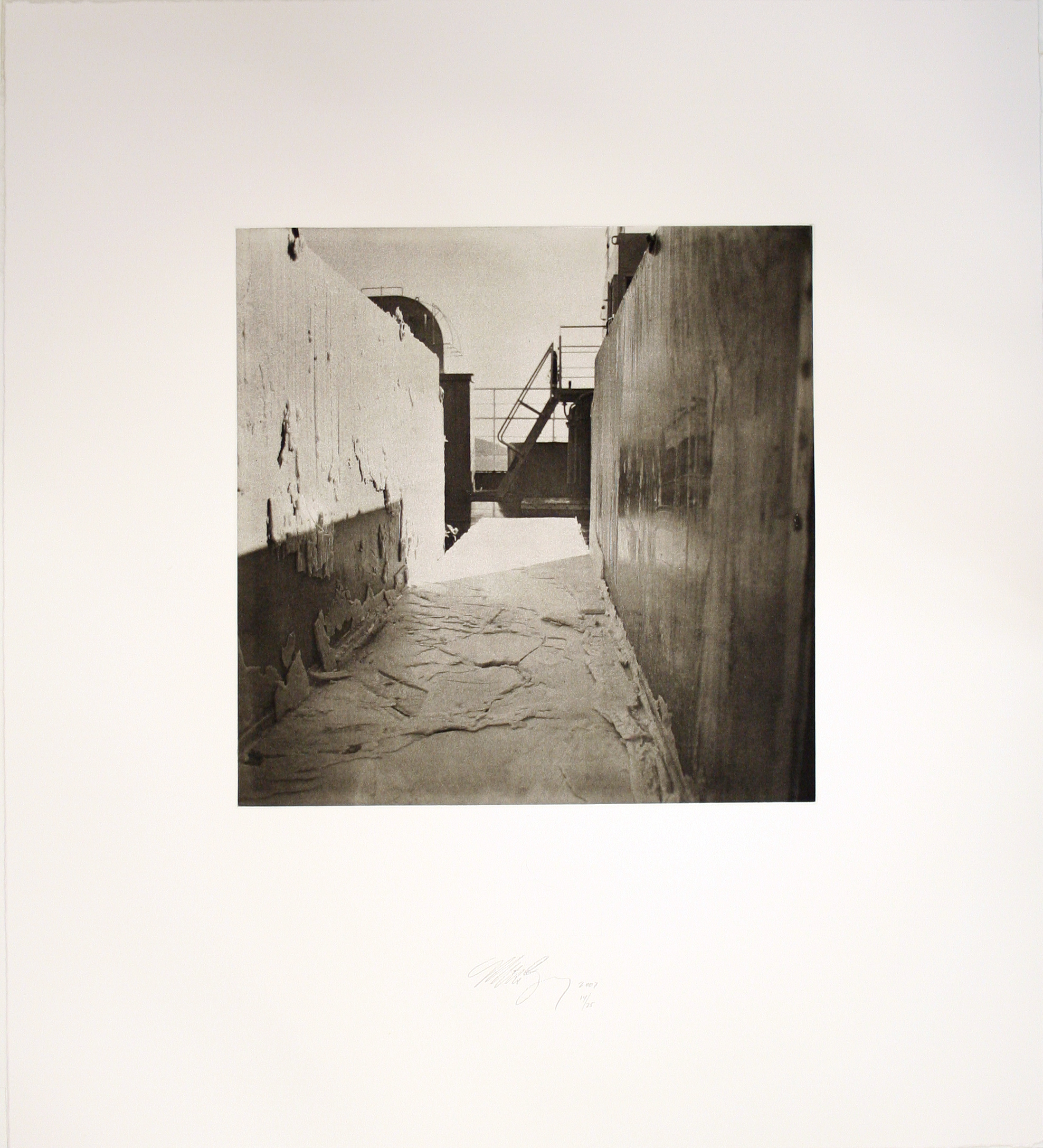 A photo features a shadowed corrridorr between two wall structures.