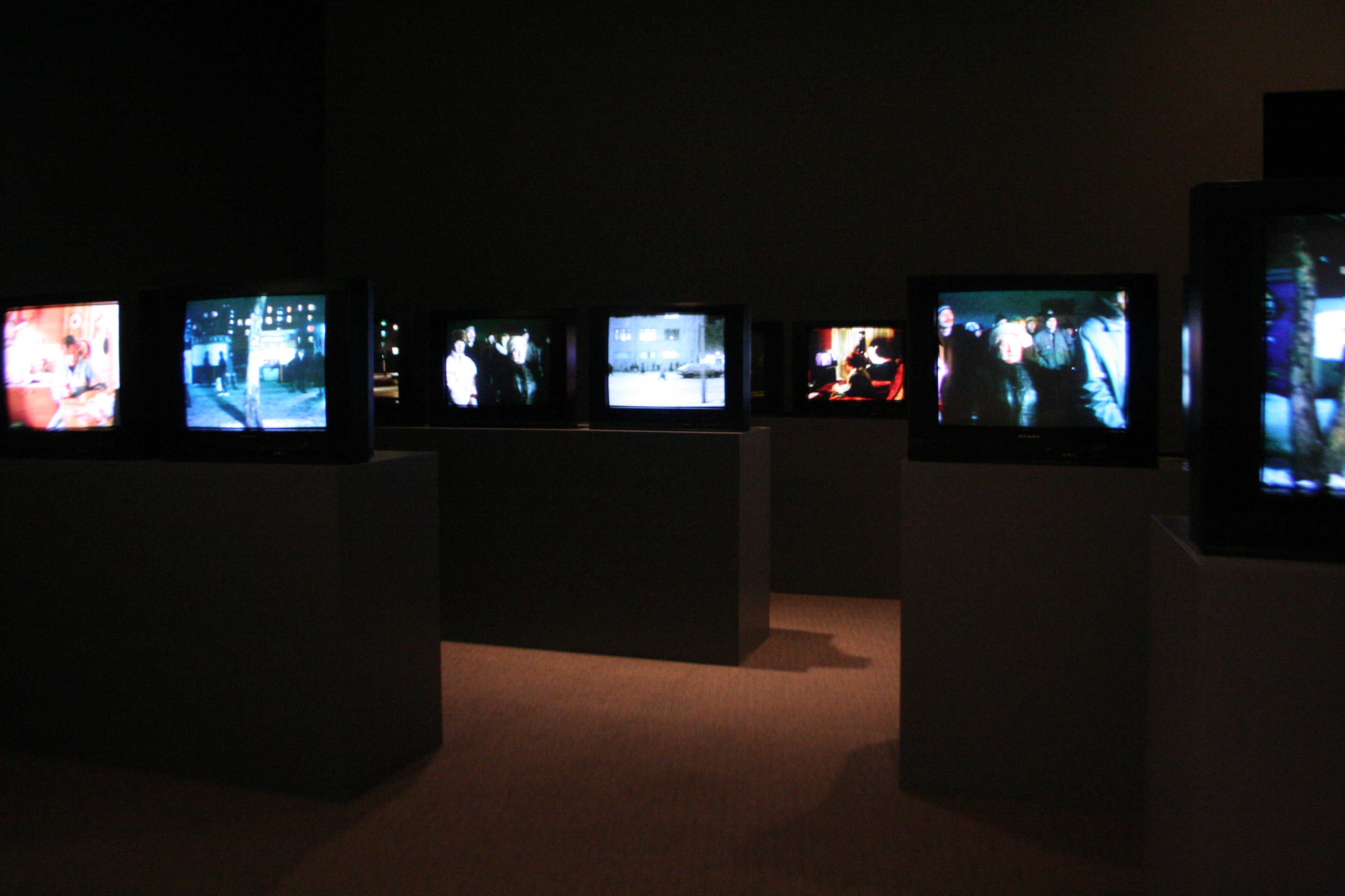 Many screens installed on podiums in a darkened gallery.