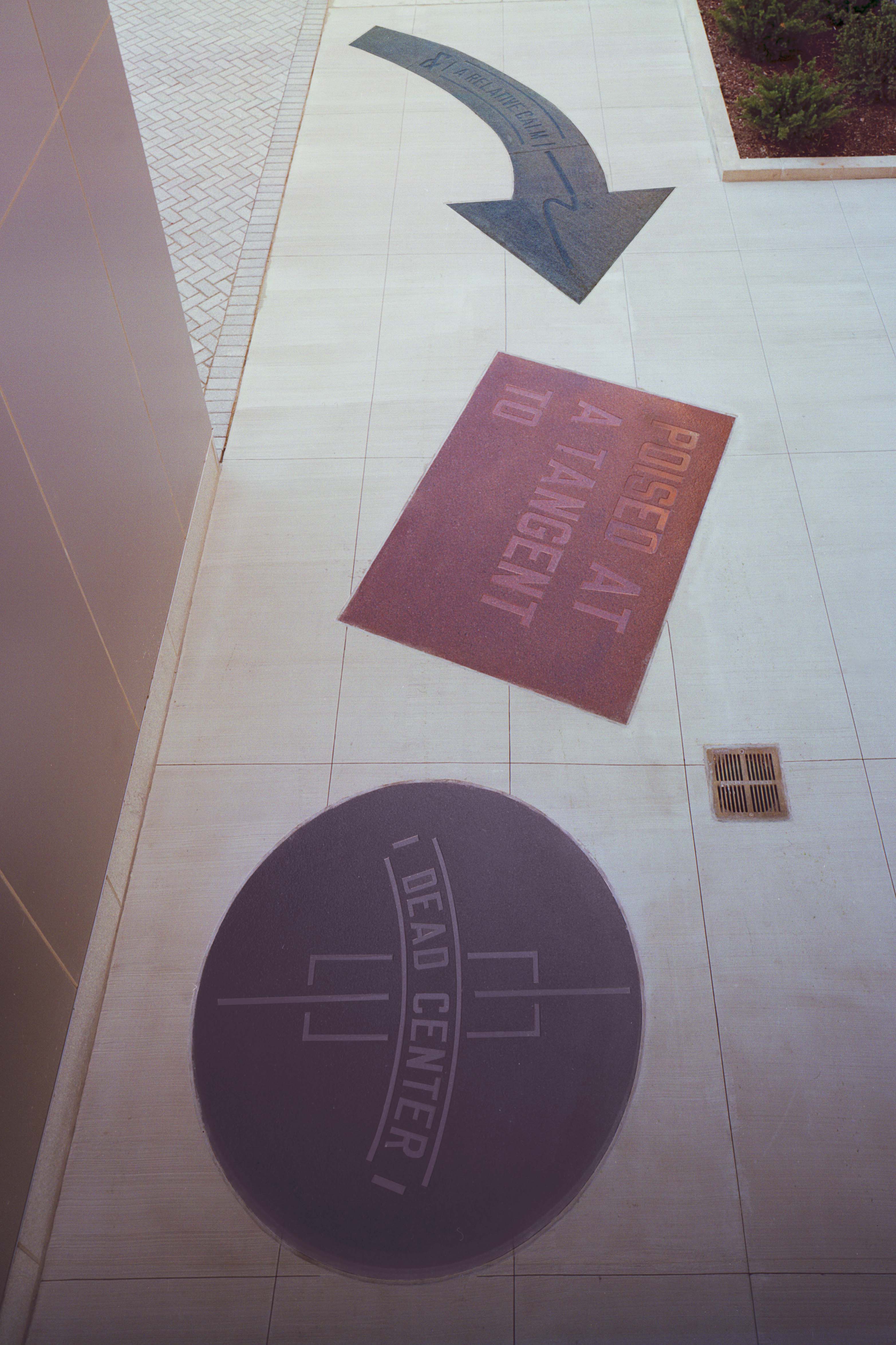 Photo of Lawrence Weiner's Dead Center includes pieces of Gray, red, and black granite that read "Dead Center" and " Poised At A Tanget To".