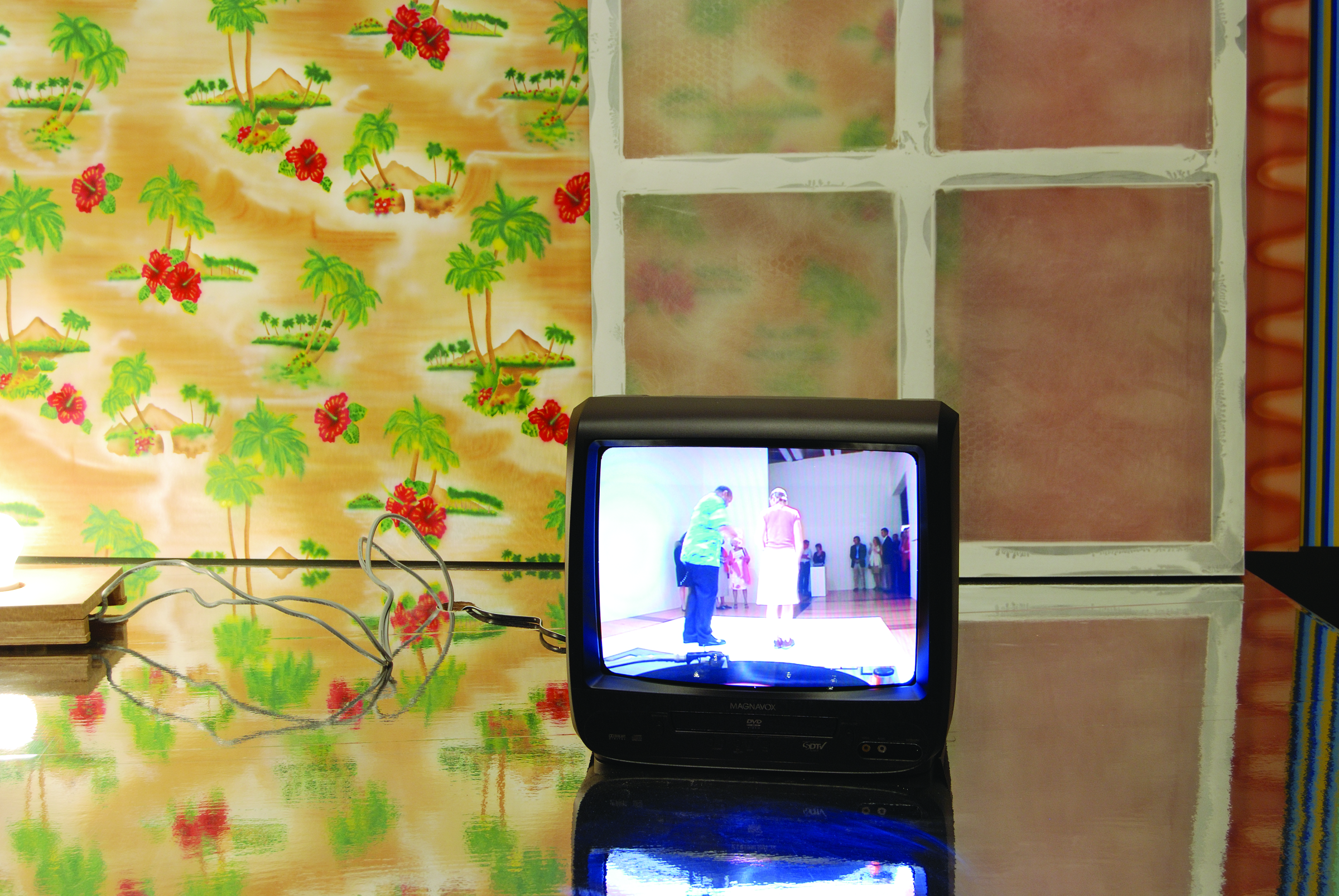 Wallpaper with red flowers and palm trees, a leaning window, and a video monitor with an image that looks like a performance