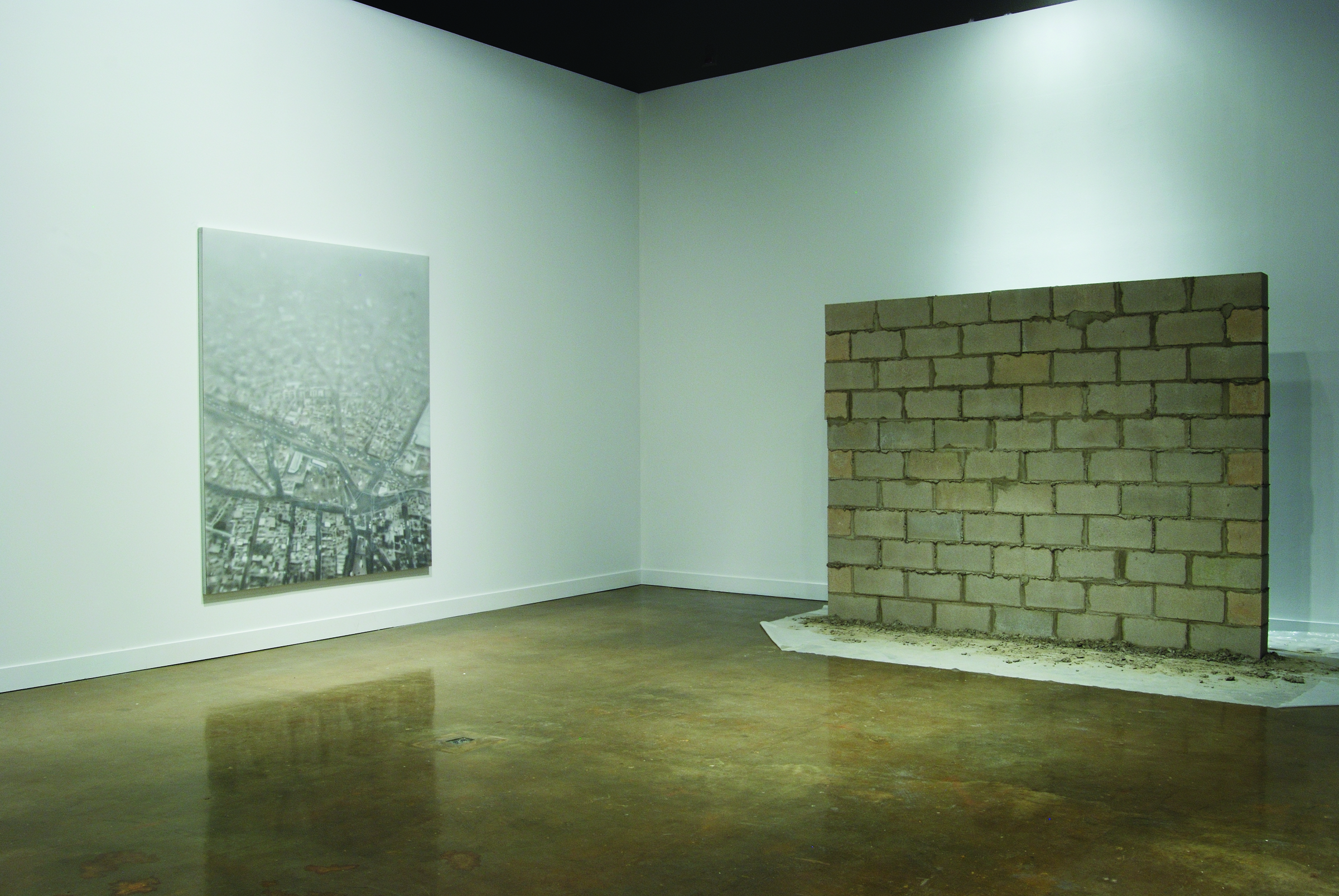A large black and white aerial view of a city on one wall, and a standing wall of concrete bricks in front of the other wall