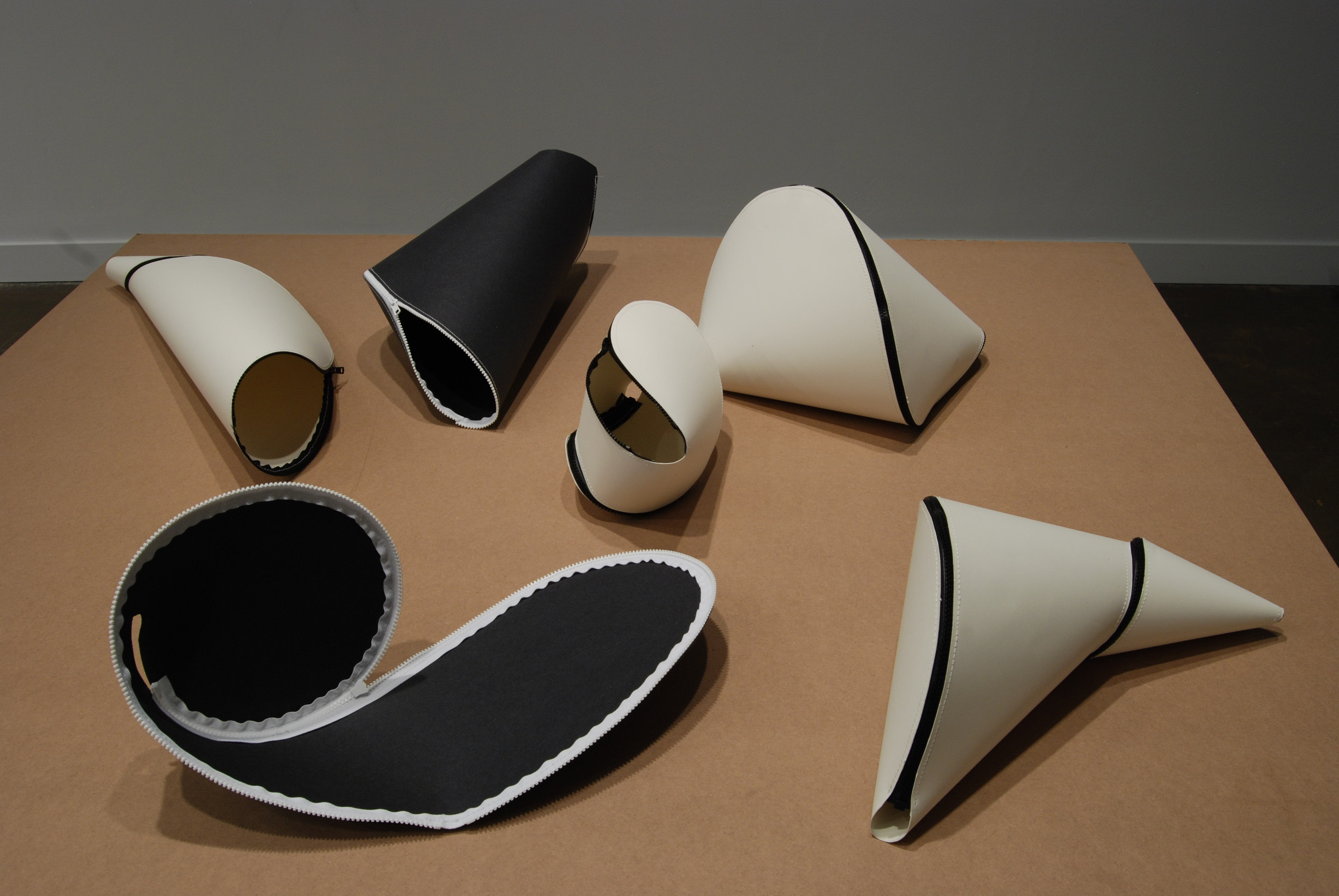 Black and white fabric sewn with zippers form geometric 3-dimensional shapes on the wood surface of a table.