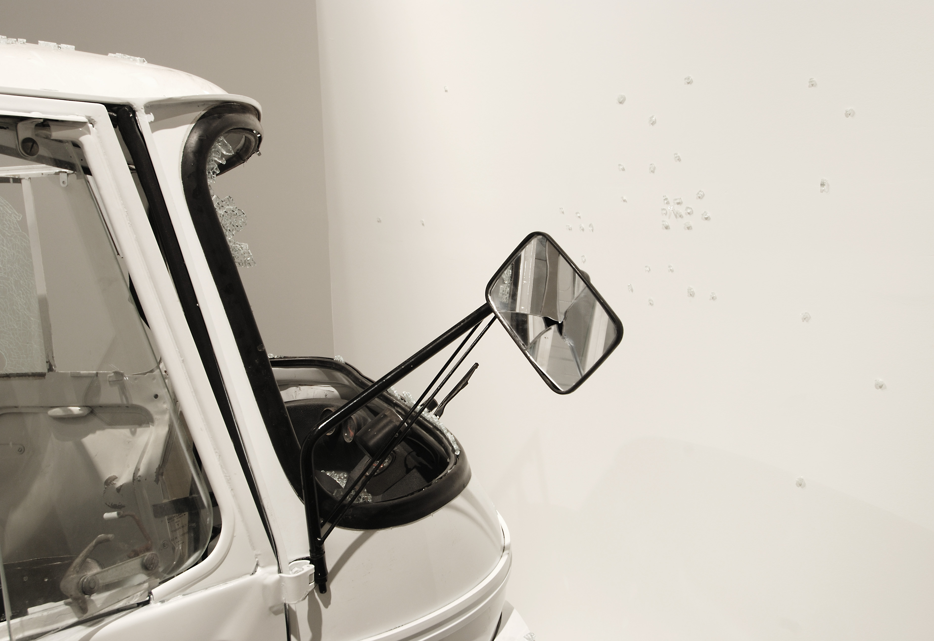 Smashed front of white Piaggio Apes vehicle with glass shards, broken windows and cracked rearview mirror