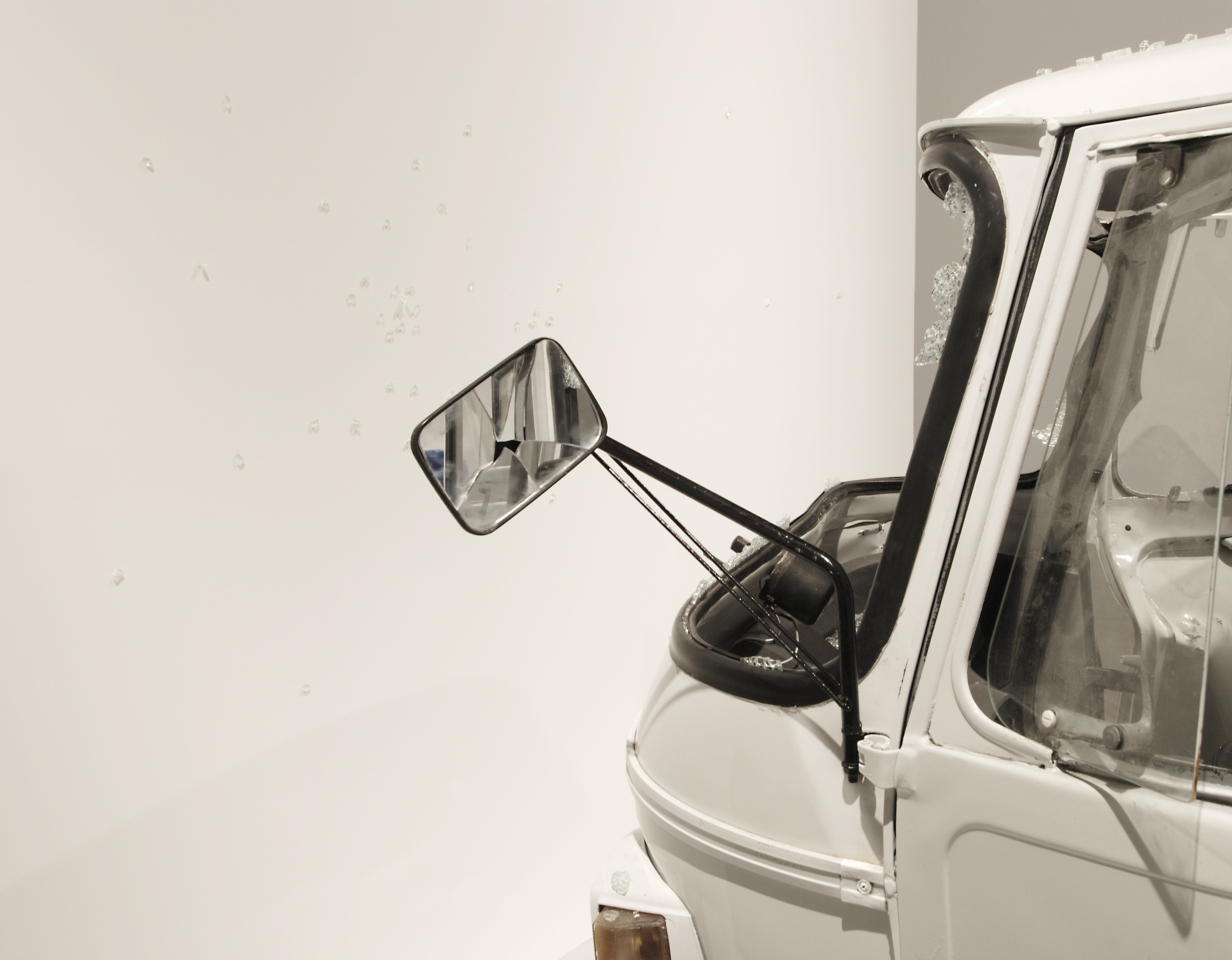 Smashed front of white Piaggio Apes vehicle with glass shards, broken windows and cracked rearview mirror