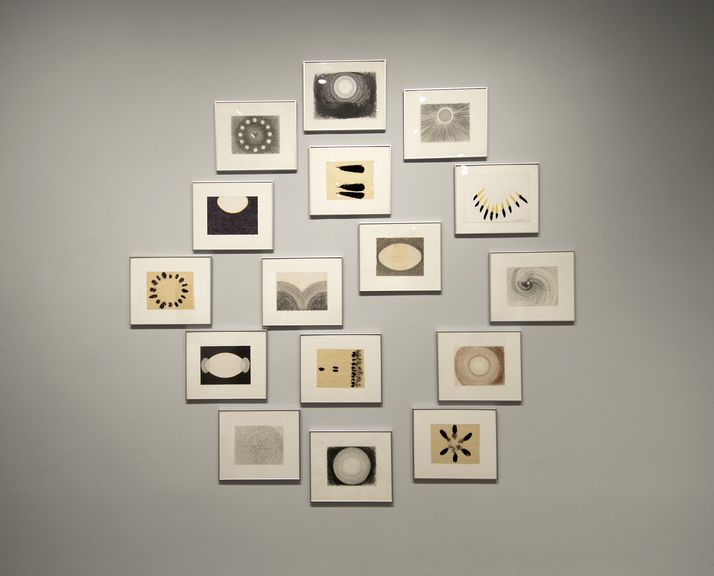 16 works of art framed and hung in a large circle.