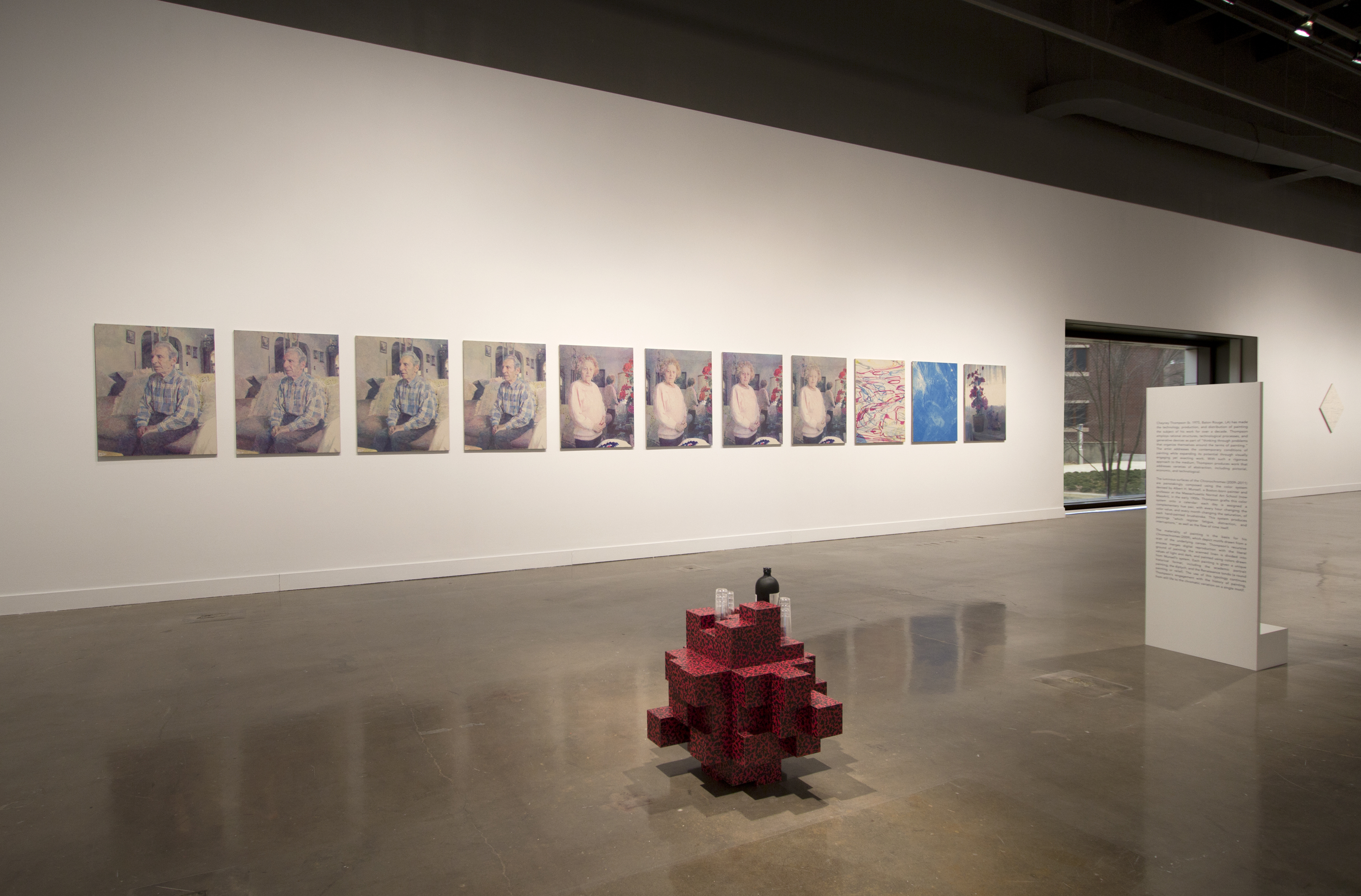 View of gallery with multipanel paintings in the back and red brick sculpture on the ground.