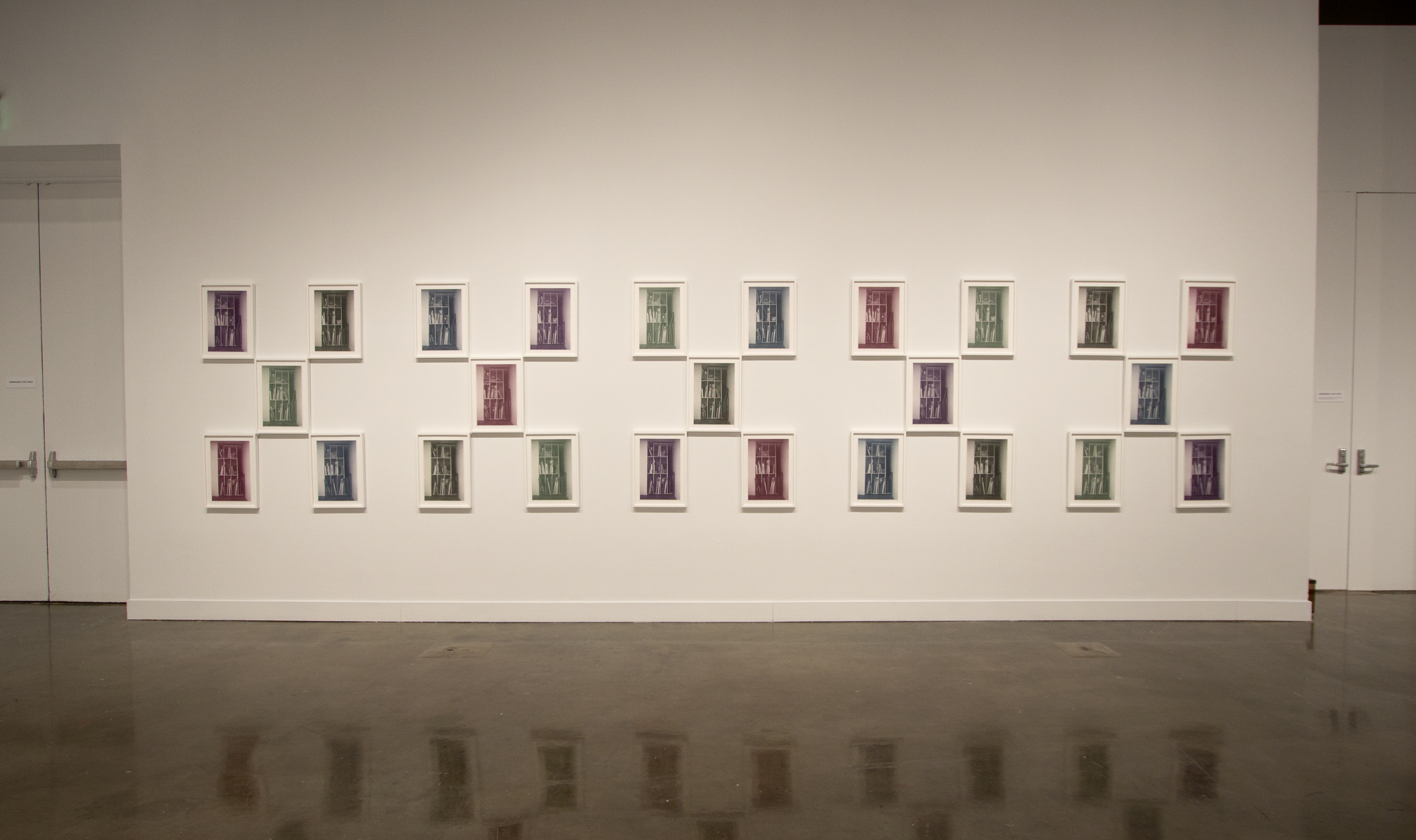 Wall with 25 small works hing in 3 symmetrical rows.