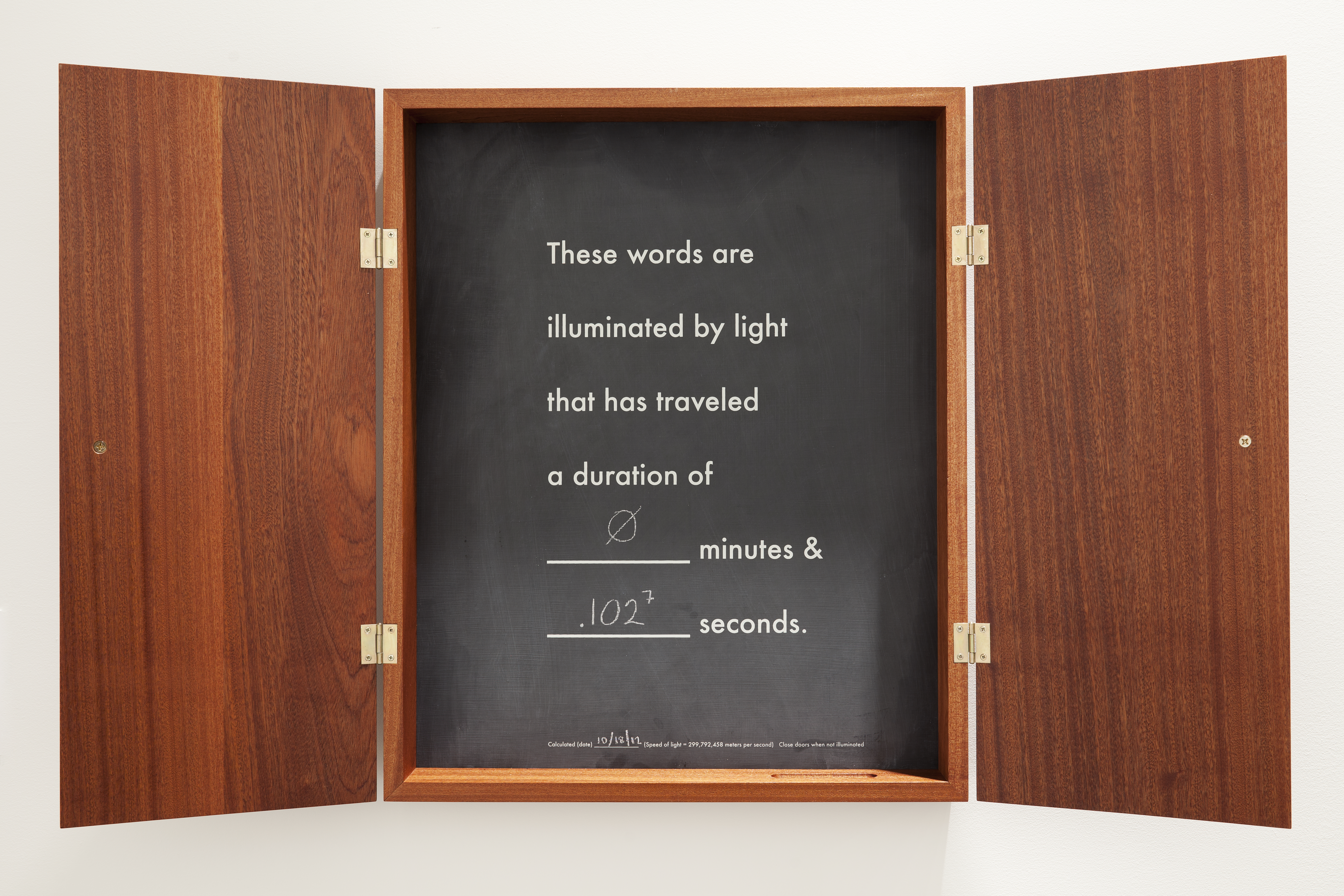 A shallow wood cabinet with chalkboard inset, the words “these words are illuminated by light that has traveled a duration of…”