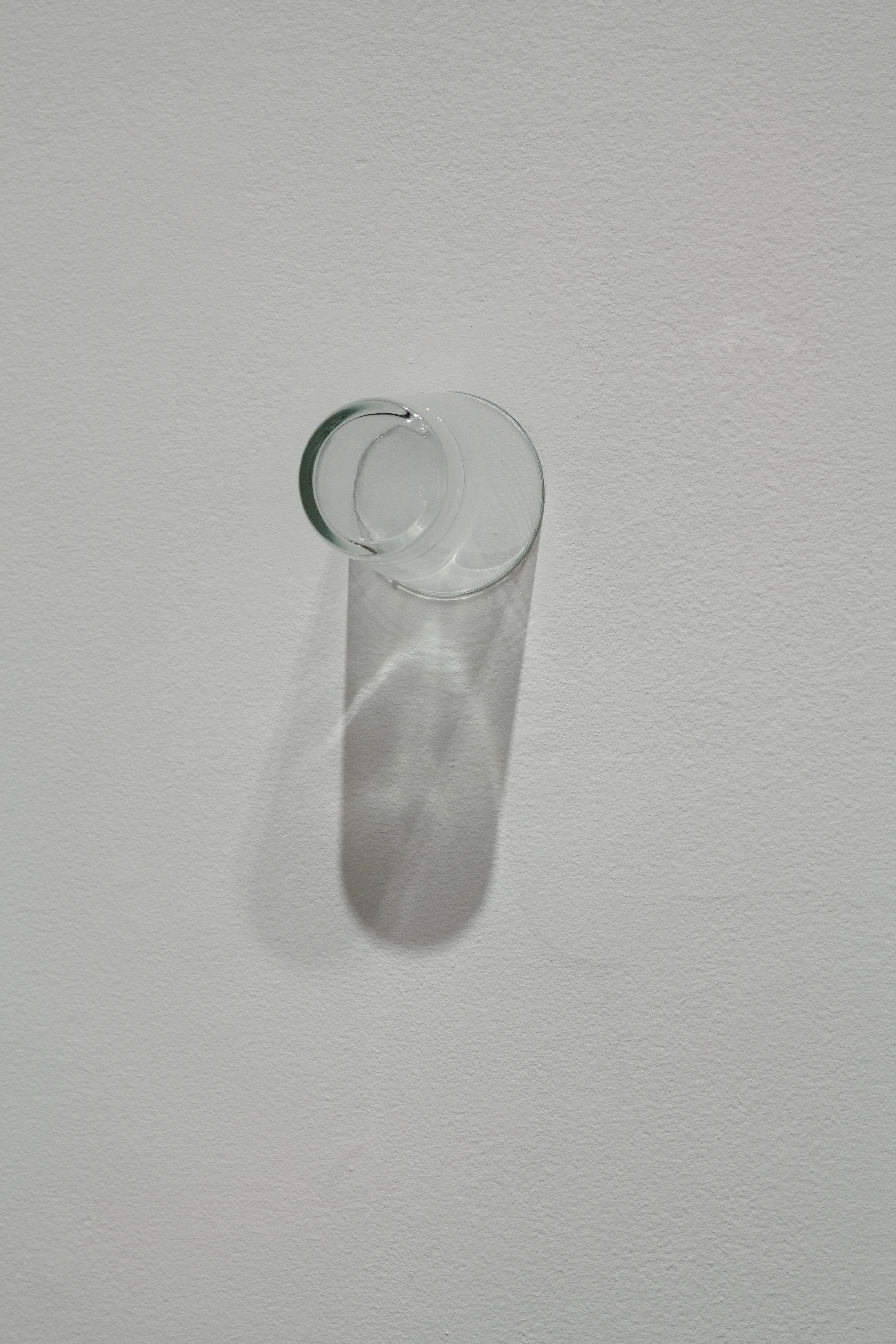 A clear drinking glass is affixed on a wall by its rim.