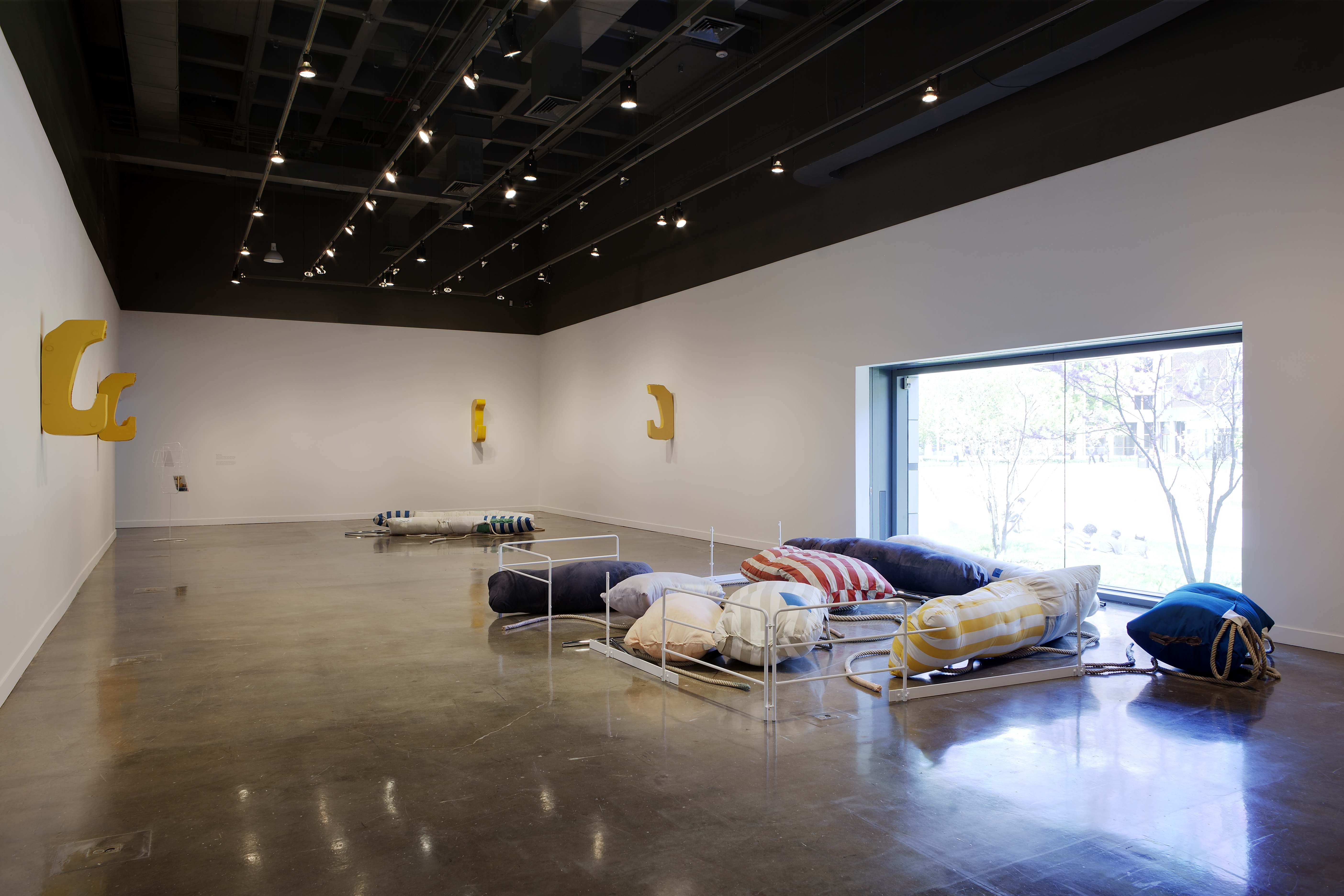 Yellow hook shaped sculptures jut from the walls, and a work composed of boldly striped pillows and gates sits on the floor.