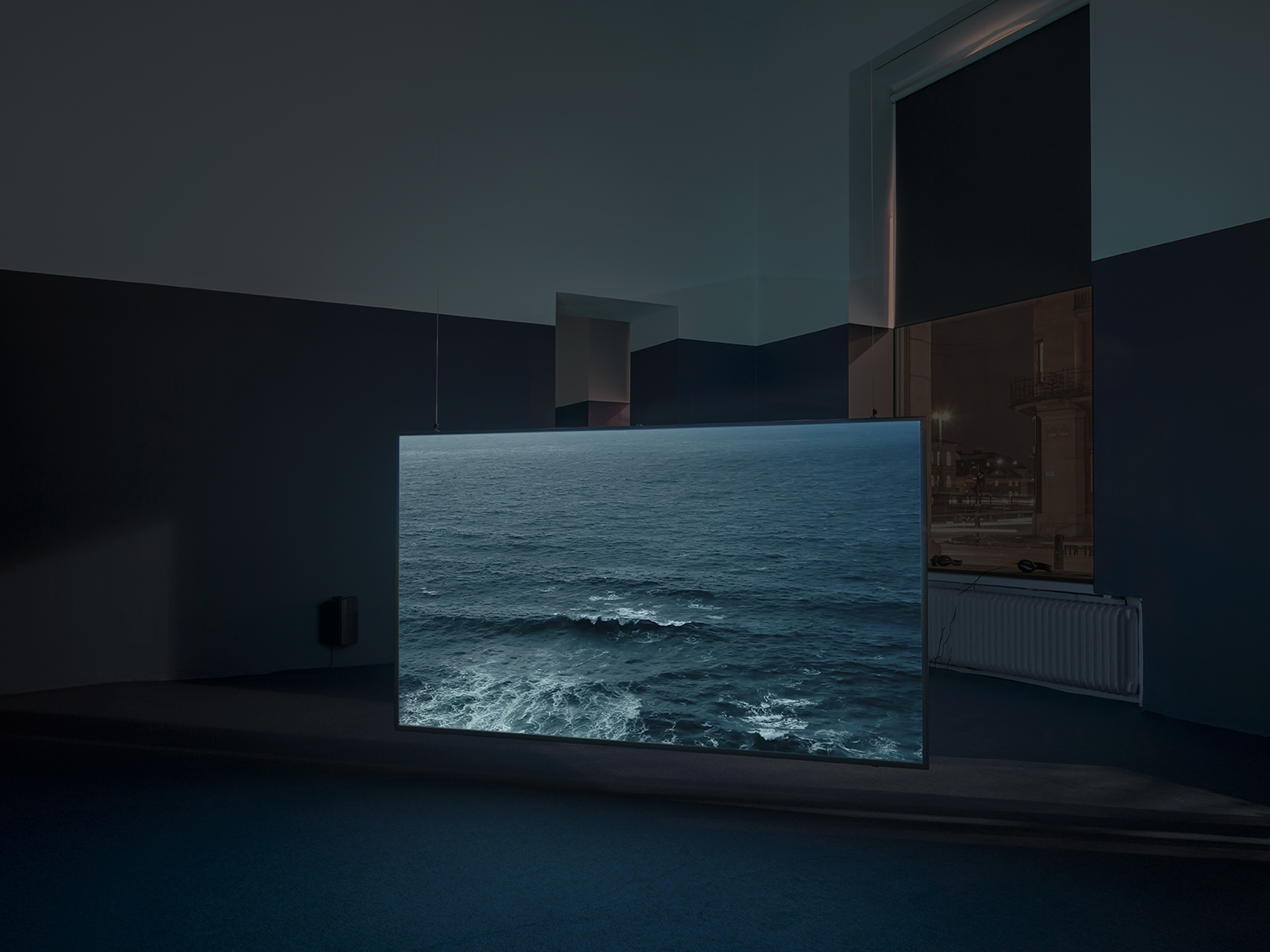 Video installation showing an ocean wave on a screen in a dim gallery.