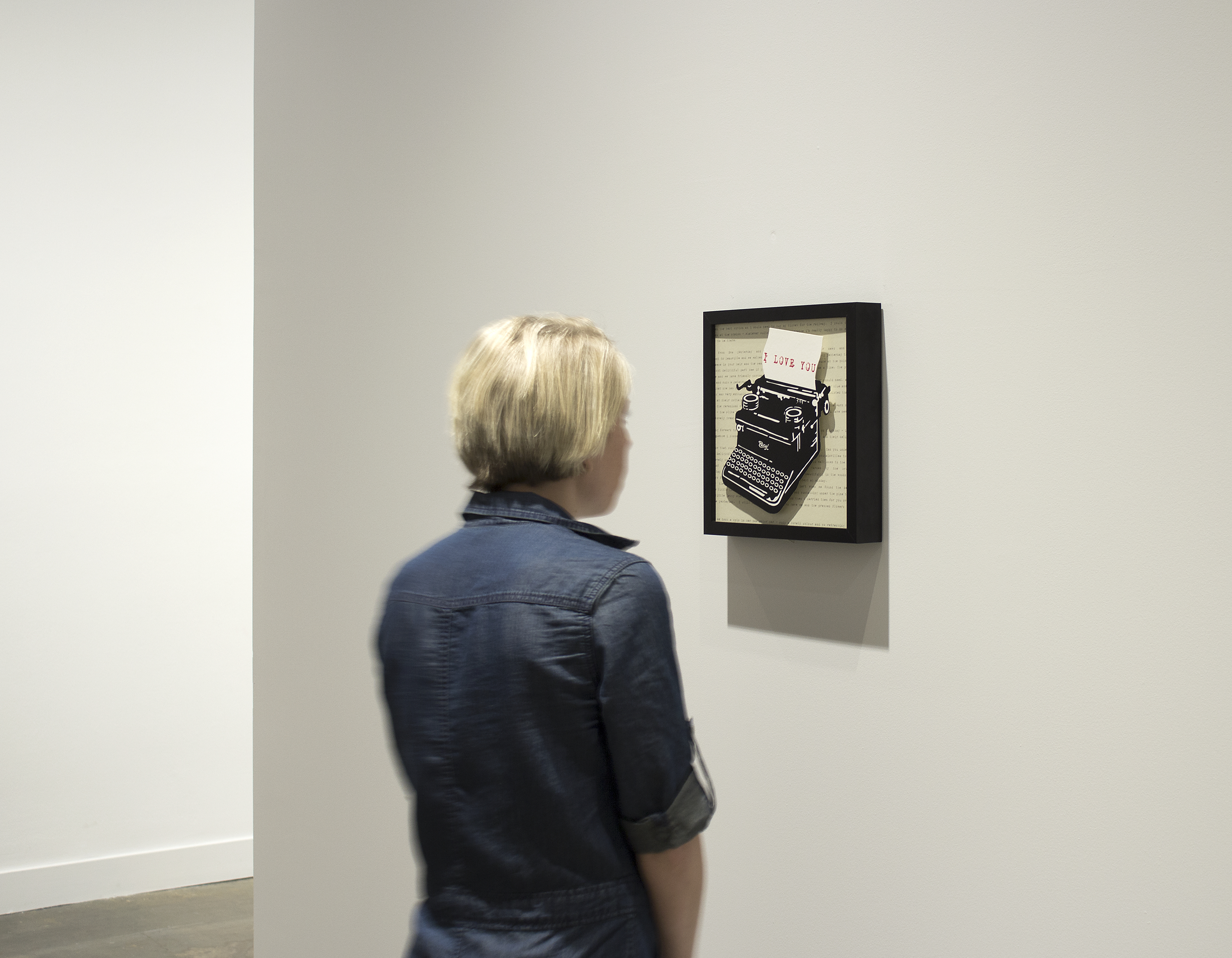 Visitor views a small framed print of an old-fashioned typewriter with a piece of paper on which “I Love You” is written.