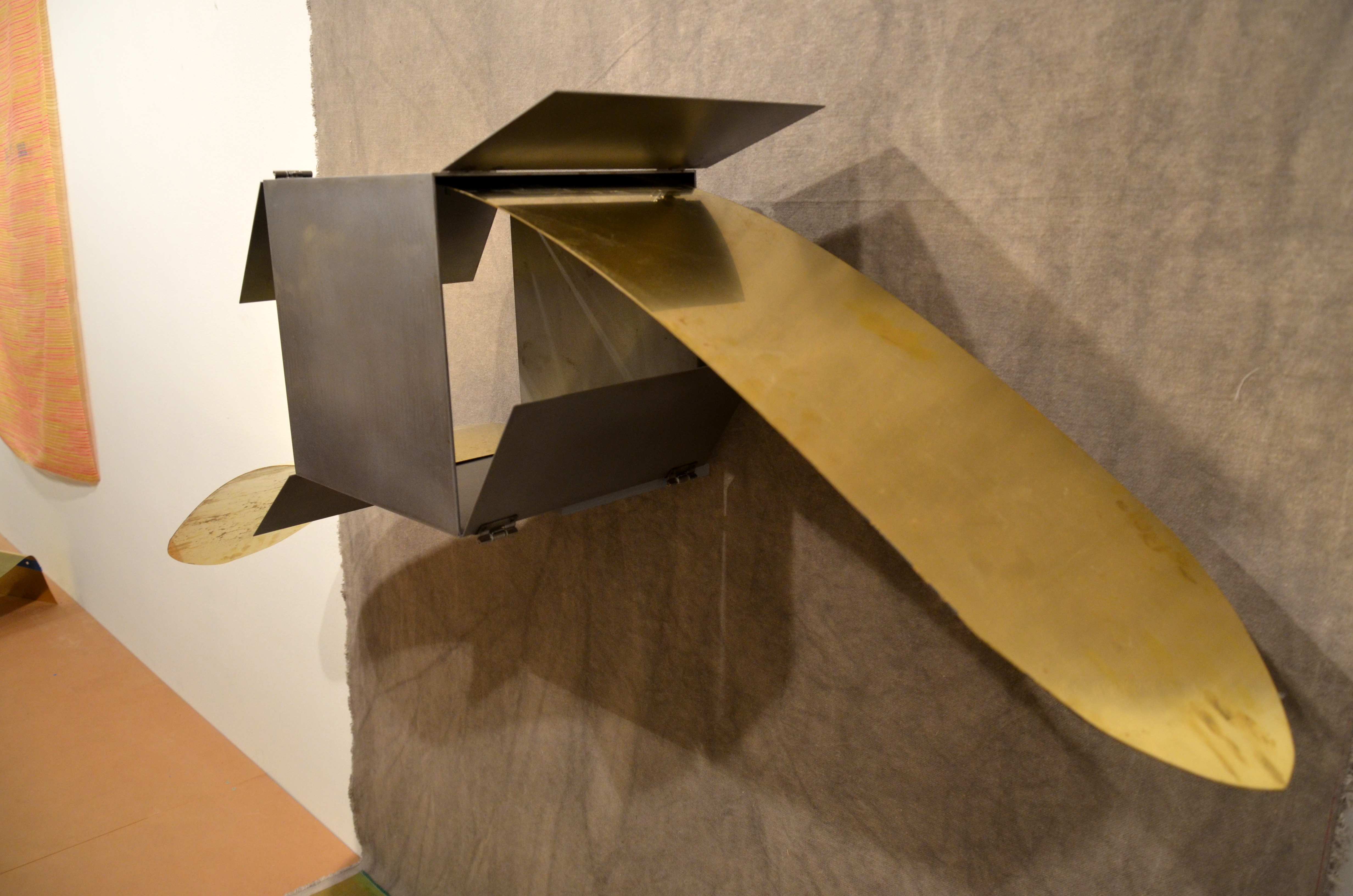 Two gold colored metal strips with curved ends extend in opposite directions from the top and bottom of an open metal box.